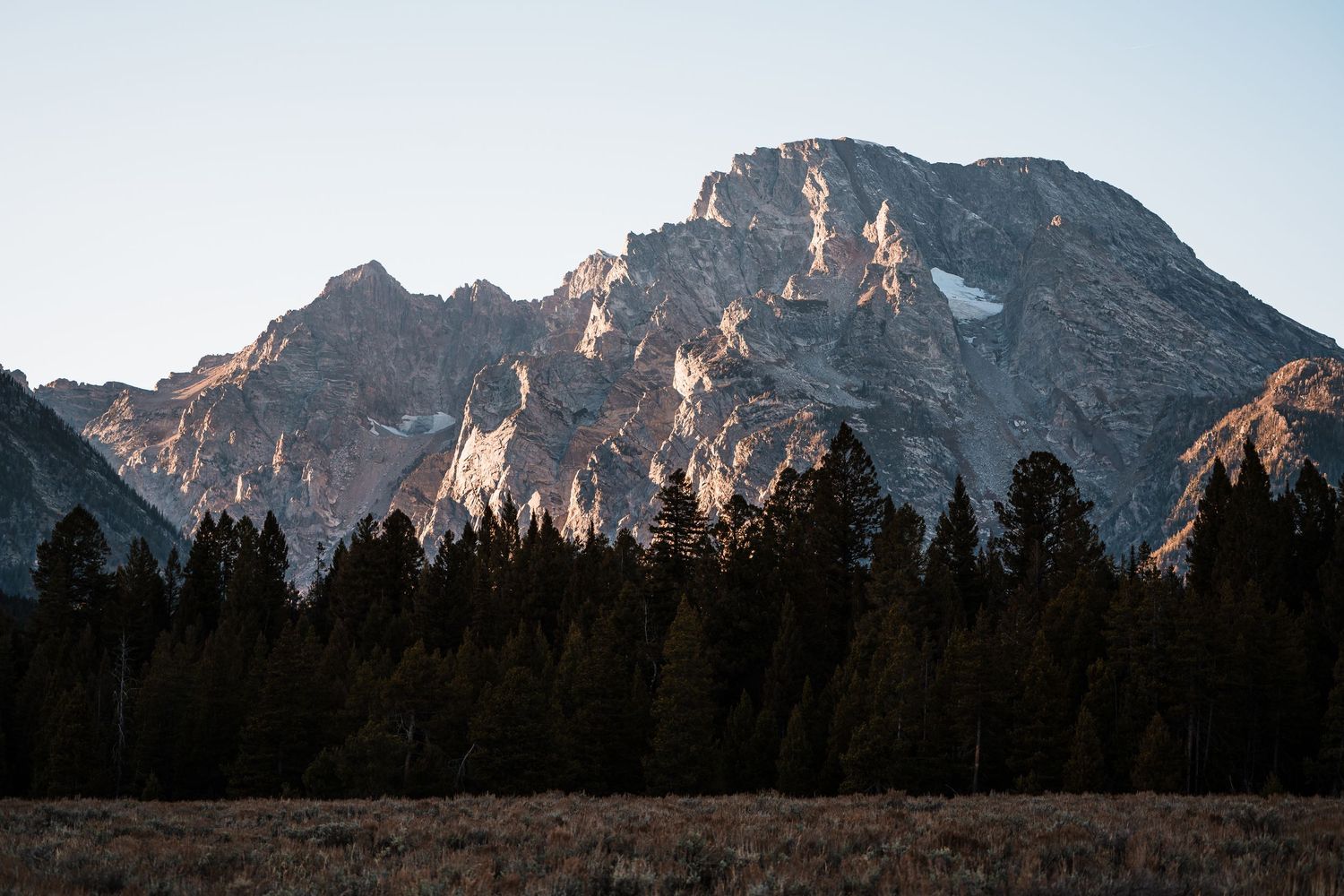 Dramatic mountain peaks rise against a cloudy sky in Grand Teton National Park during autumn.