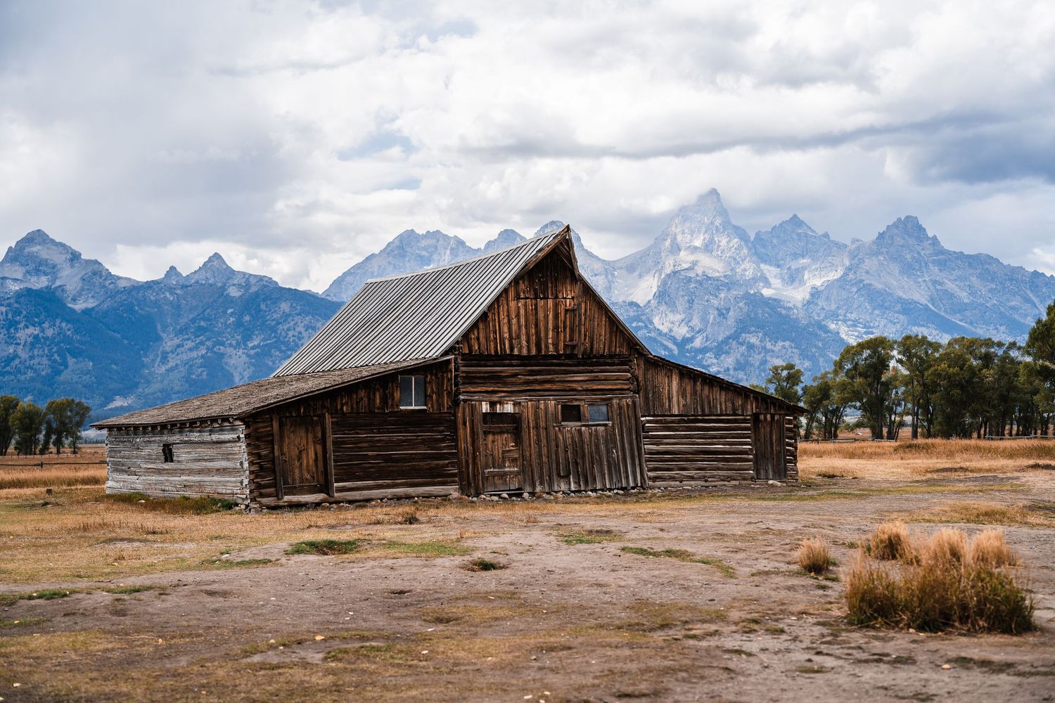 Historic wooden Mormon Row barns with dramatic Grand Teton mountain range backdrop in Wyoming.
