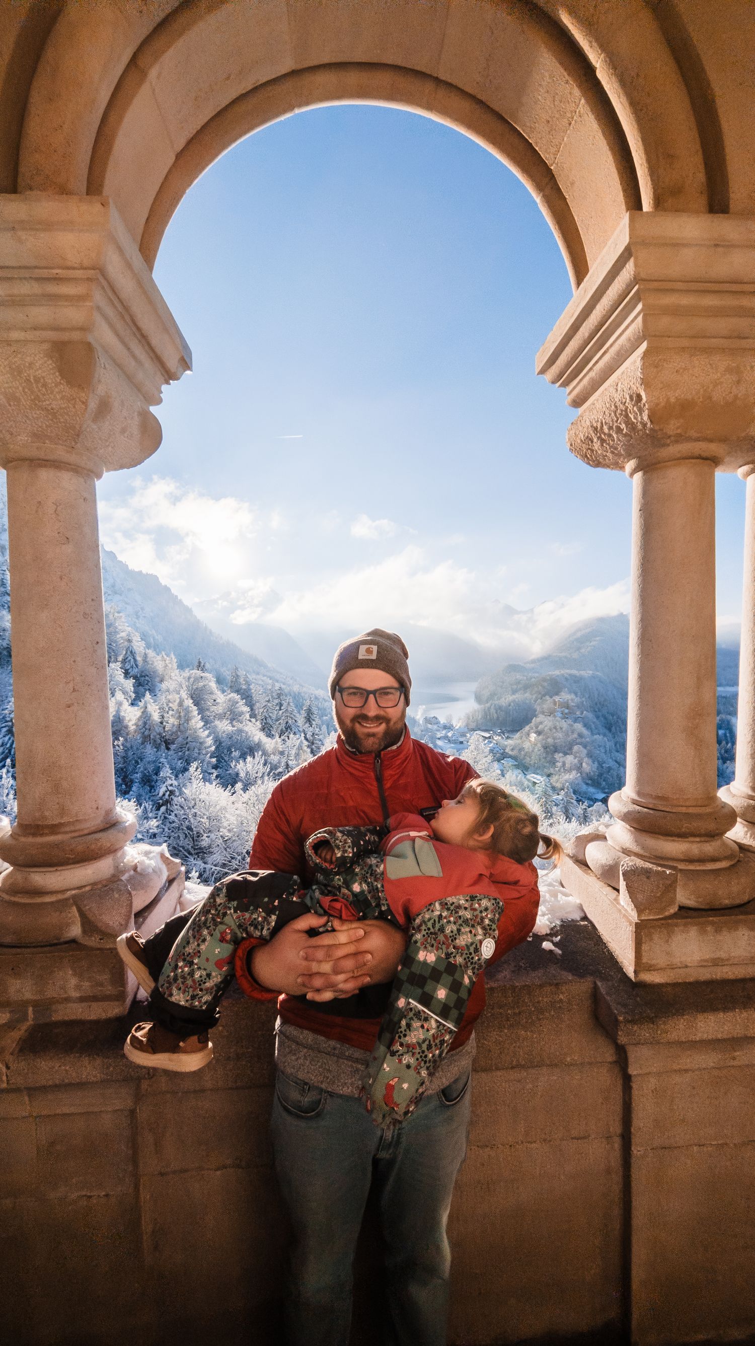 Stone archways frame a scenic mountain vista with snow-covered peaks against a bright blue sky.