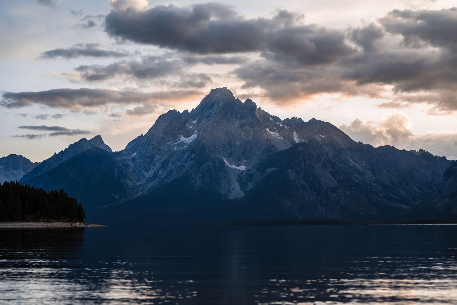 A panoramic view of snow-capped mountains reflecting in Jackson Lake at Grand Teton National Park during sunset.