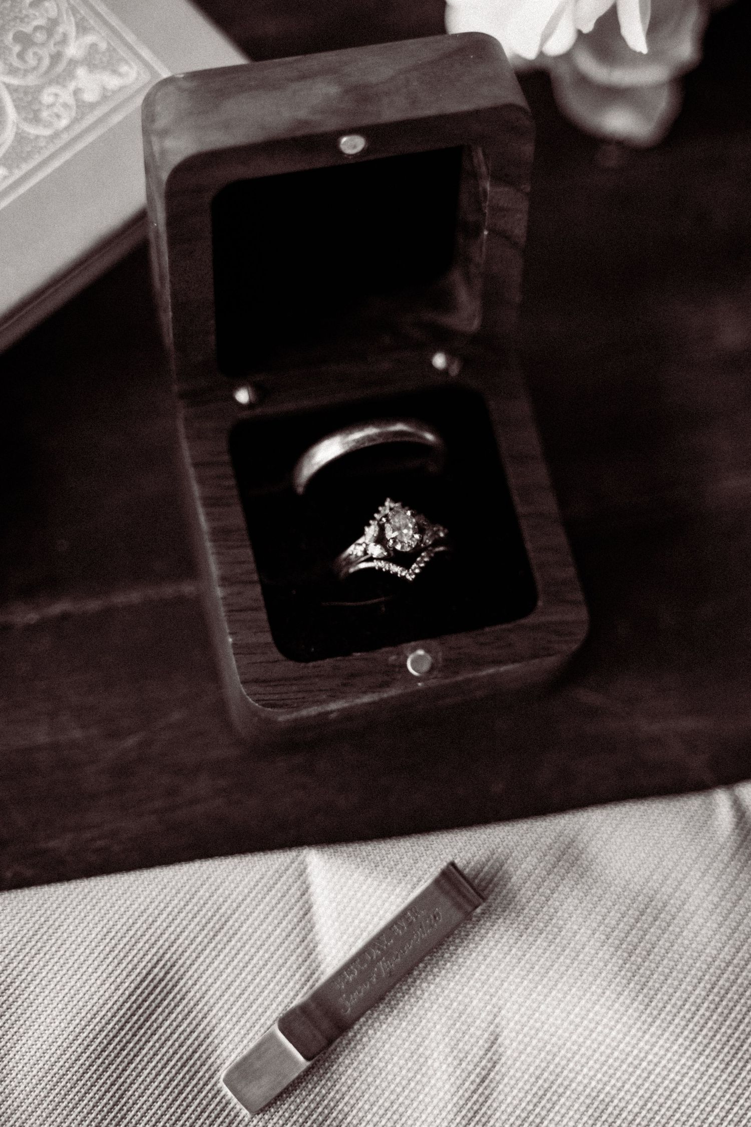 Black and white photo of wedding rings in a wooden velvet-lined box on a textured surface.