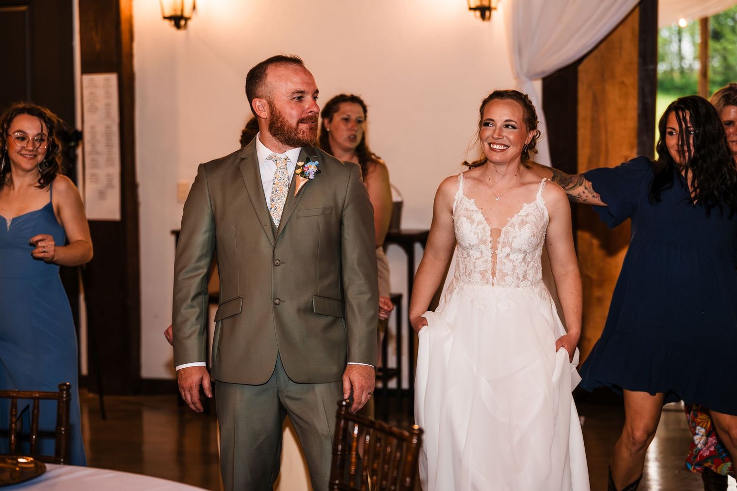 Bride in lace gown and groom in tan suit make grand reception entrance.