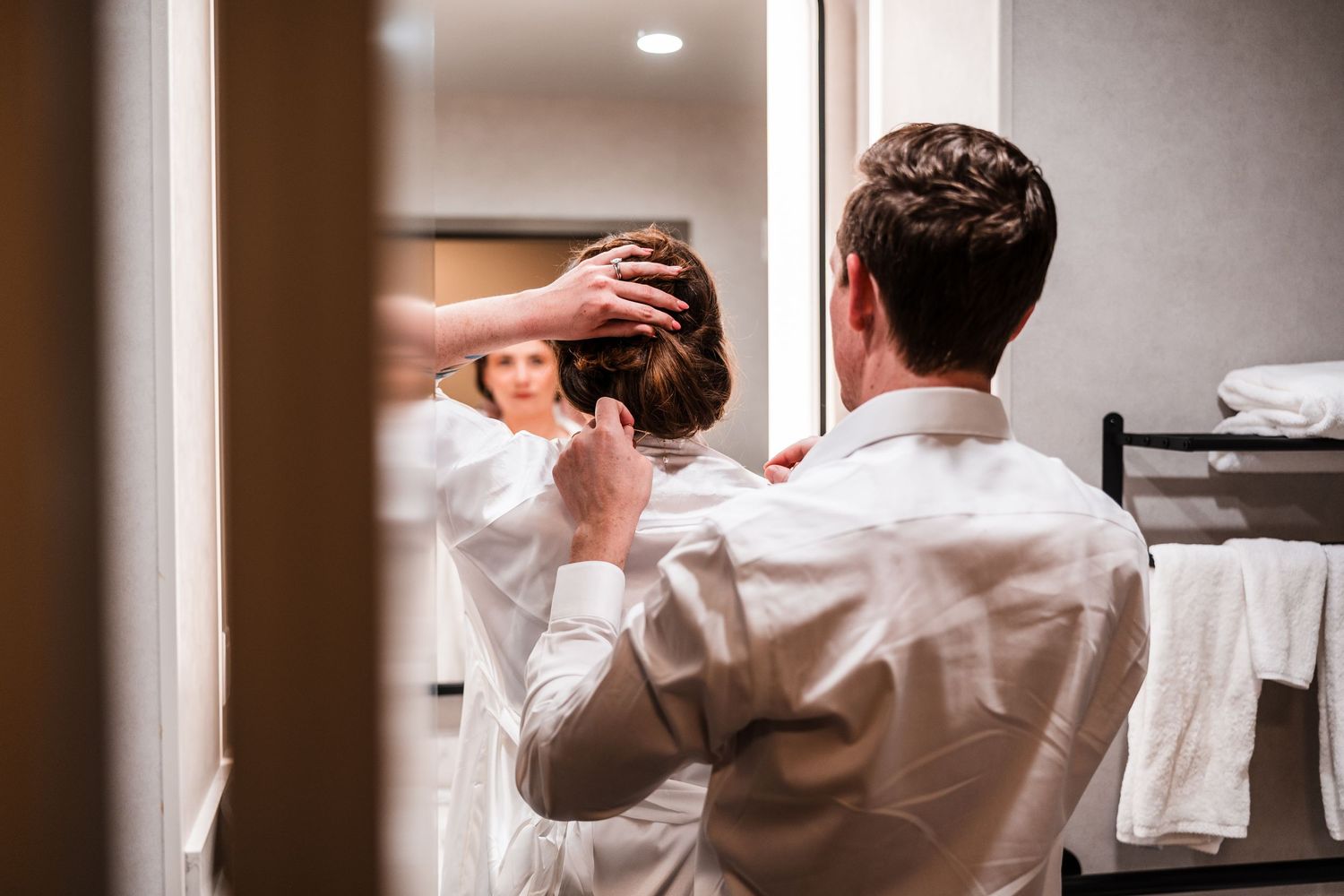A man in a white dress shirt getting his hair styled by a woman, reflected in a mirror.