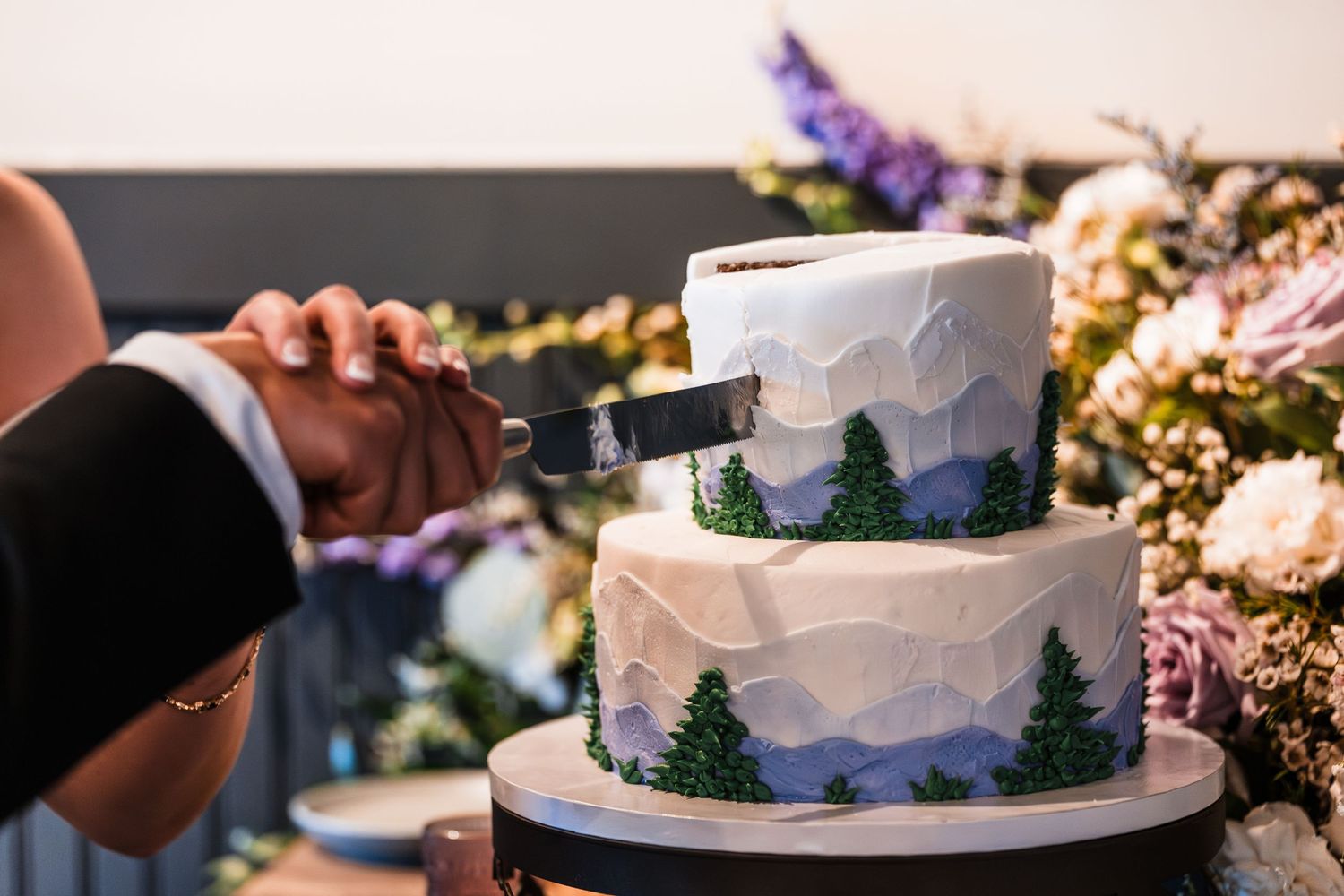 Bride and groom cutting a two-tier mountain-themed wedding cake with pine tree design.