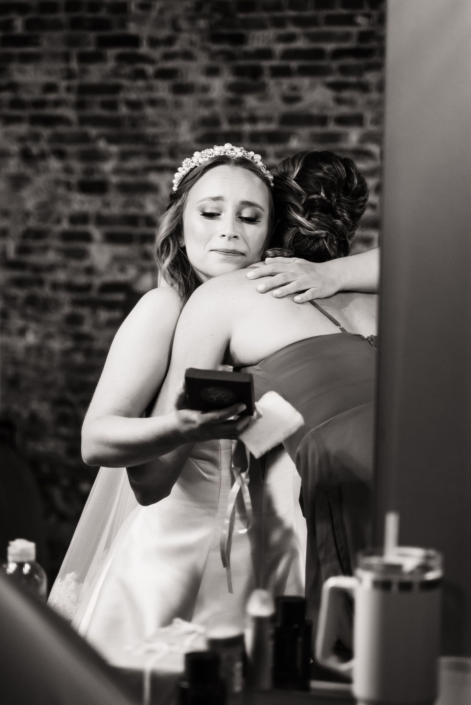 Black and white candid moment captured against exposed brick wall during wedding preparations.