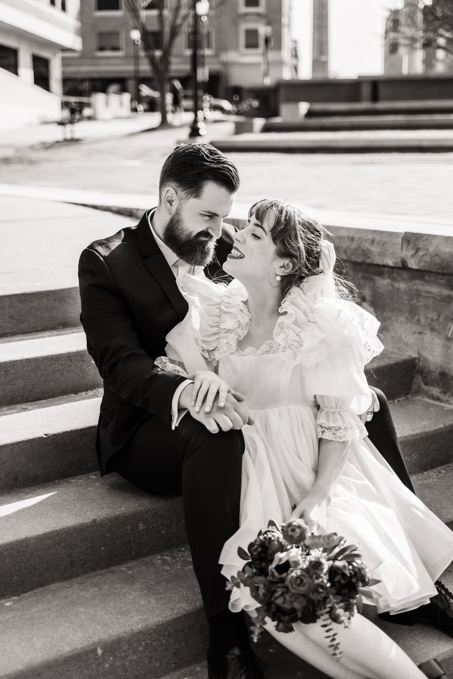Black and white photo of a couple sharing an intimate moment while sitting on outdoor steps.