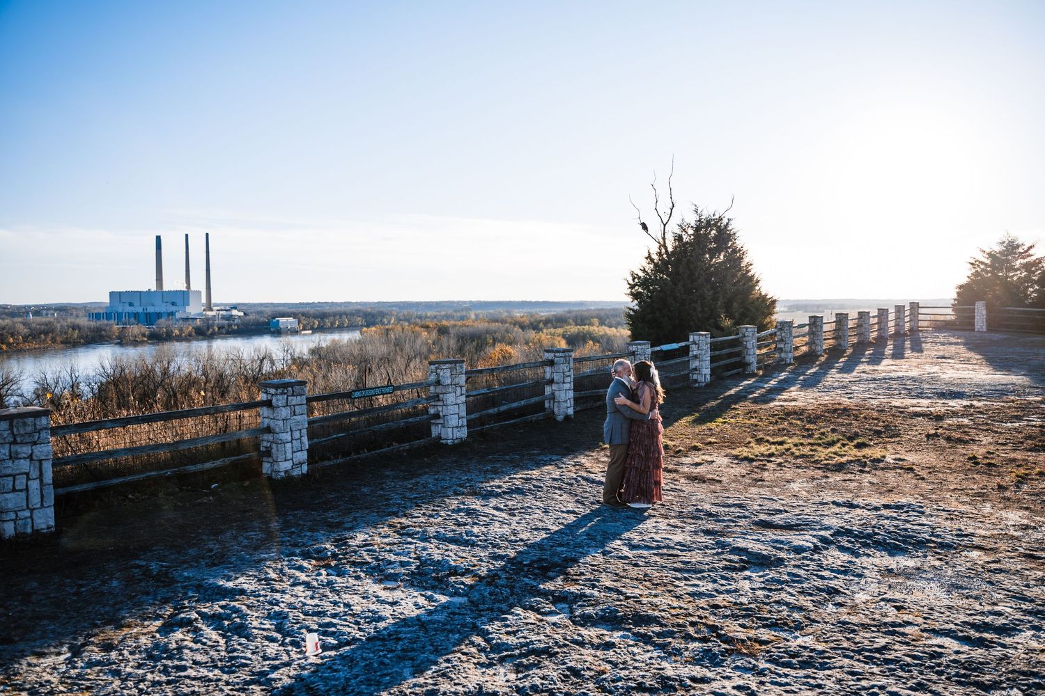 Stone wall path with industrial buildings and smokestacks visible in the distance on a clear winter day.