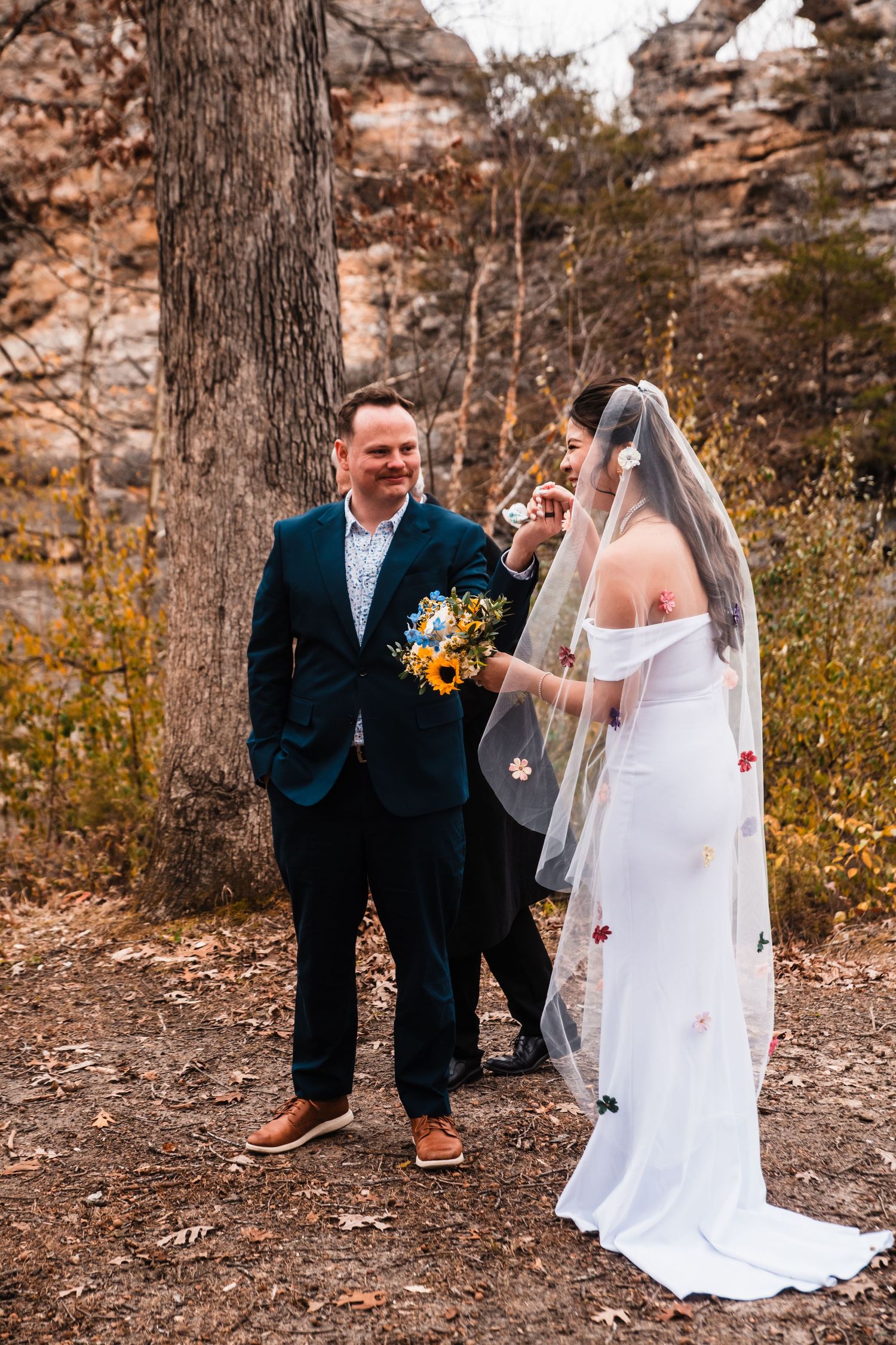 Candid moment between newlyweds during autumn wedding with sunflowers and natural rock formations.