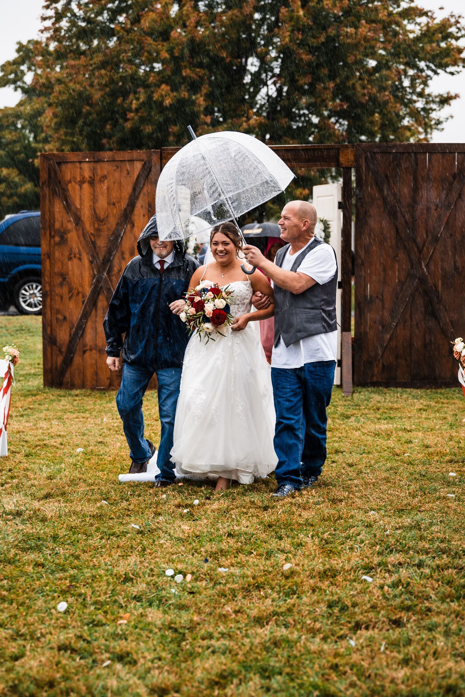 Wedding party members walking across grass field during outdoor autumn ceremony.
