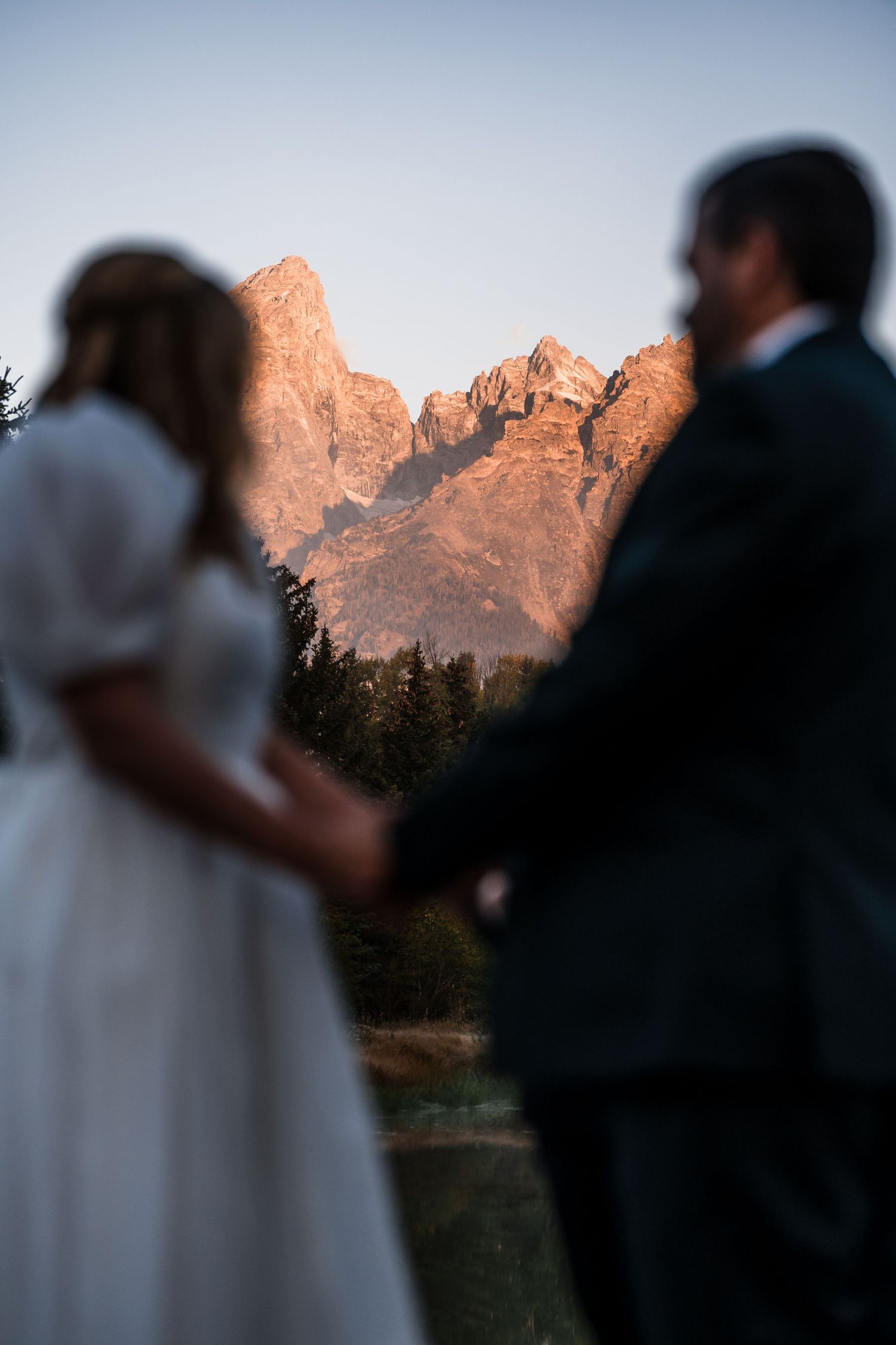 Silhouetted figures against a sunset-lit mountain range during an outdoor wedding ceremony.
