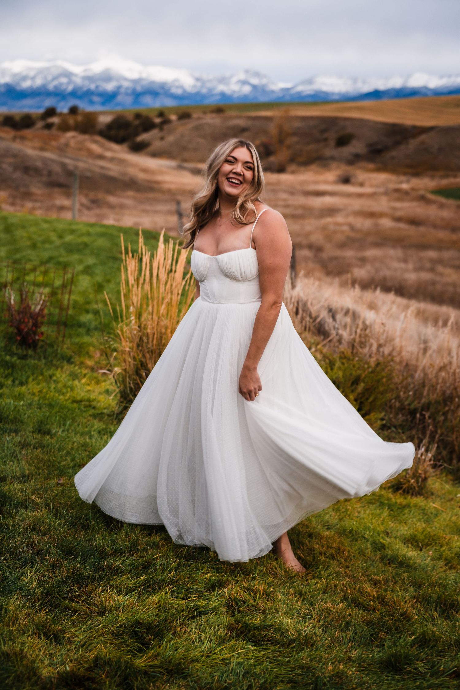 A flowing white wedding dress twirls gracefully against a mountainous landscape at sunset.