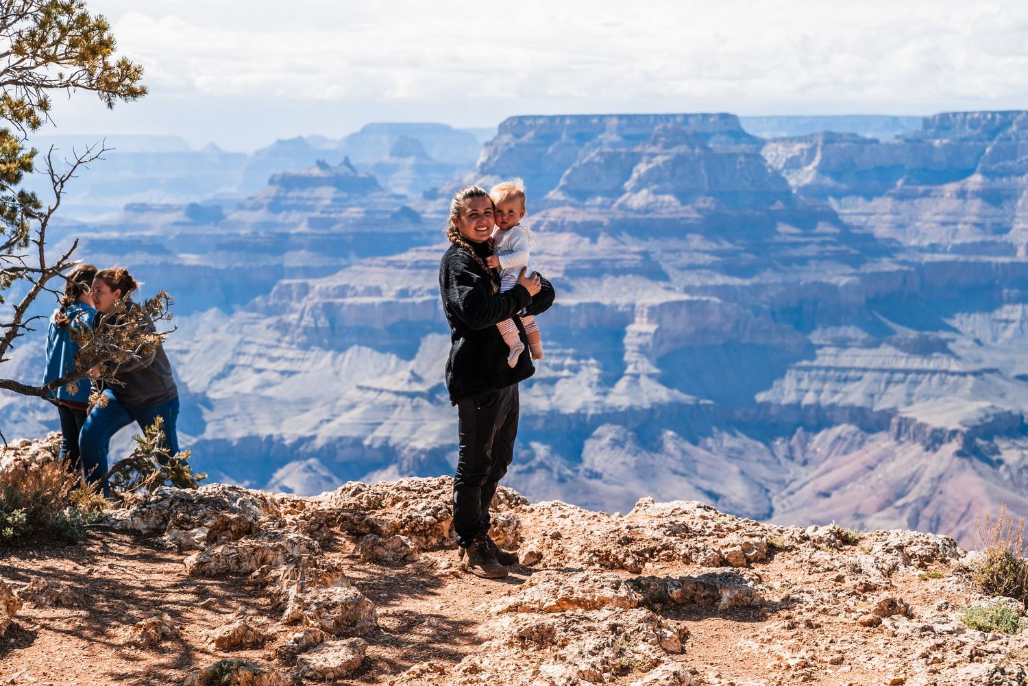 A visitor holds a small child while enjoying the breathtaking view at the Grand Canyon's edge.
