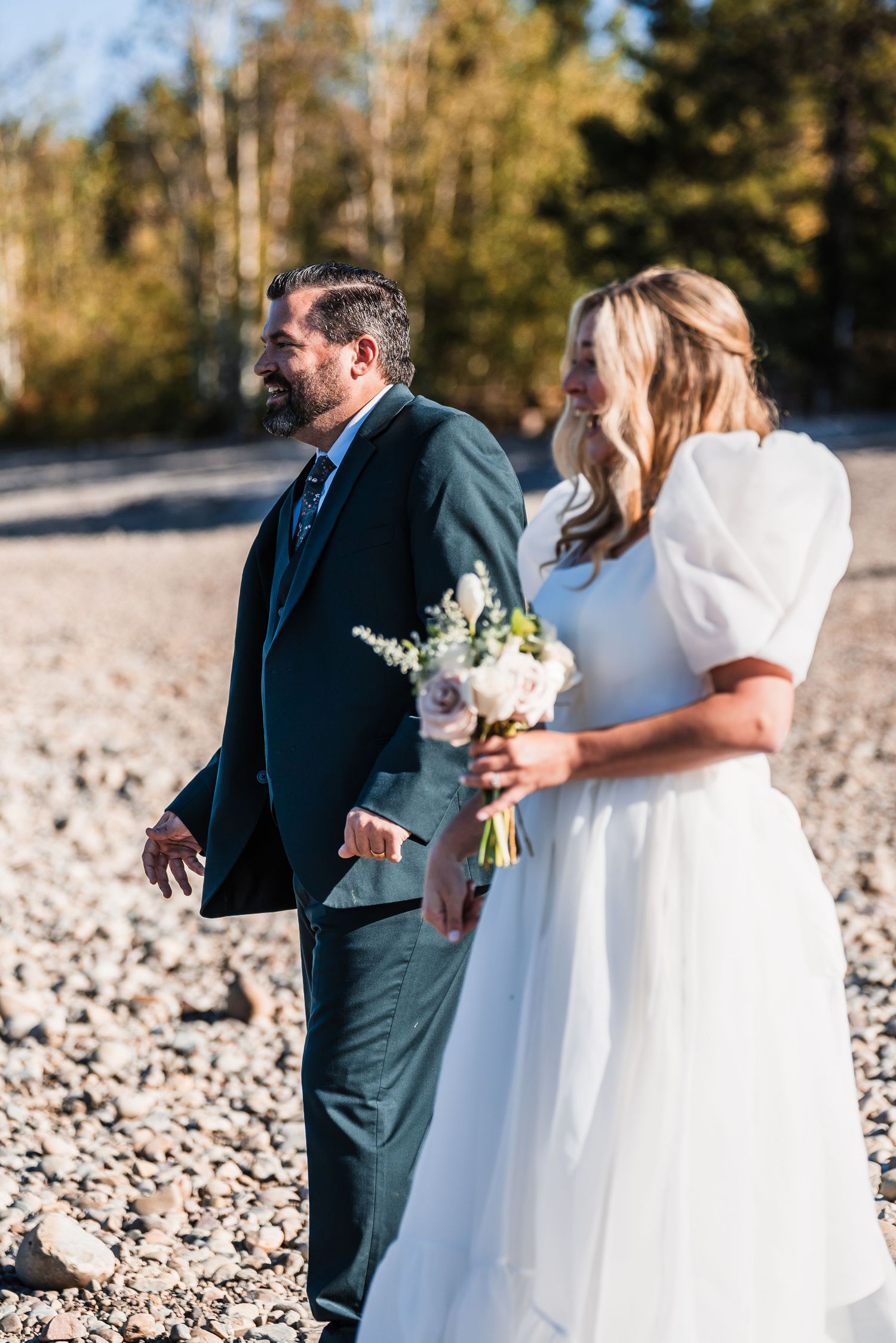 Wedding party gathered on a rocky beach with snow-capped mountains in the distance.