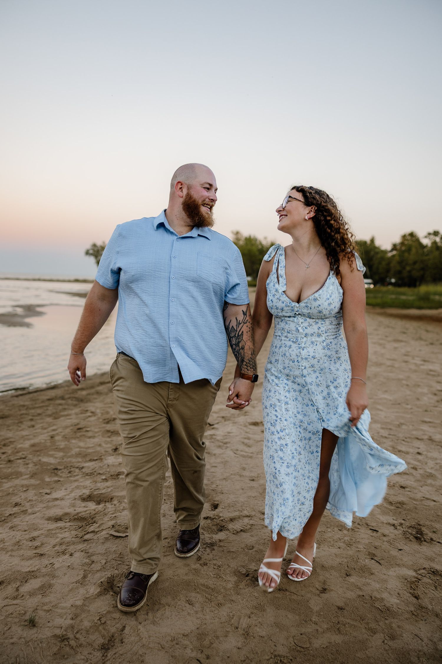 Beach engagement walking, looking at each other and kissing on beach golden hour Marquette, Michigan.
