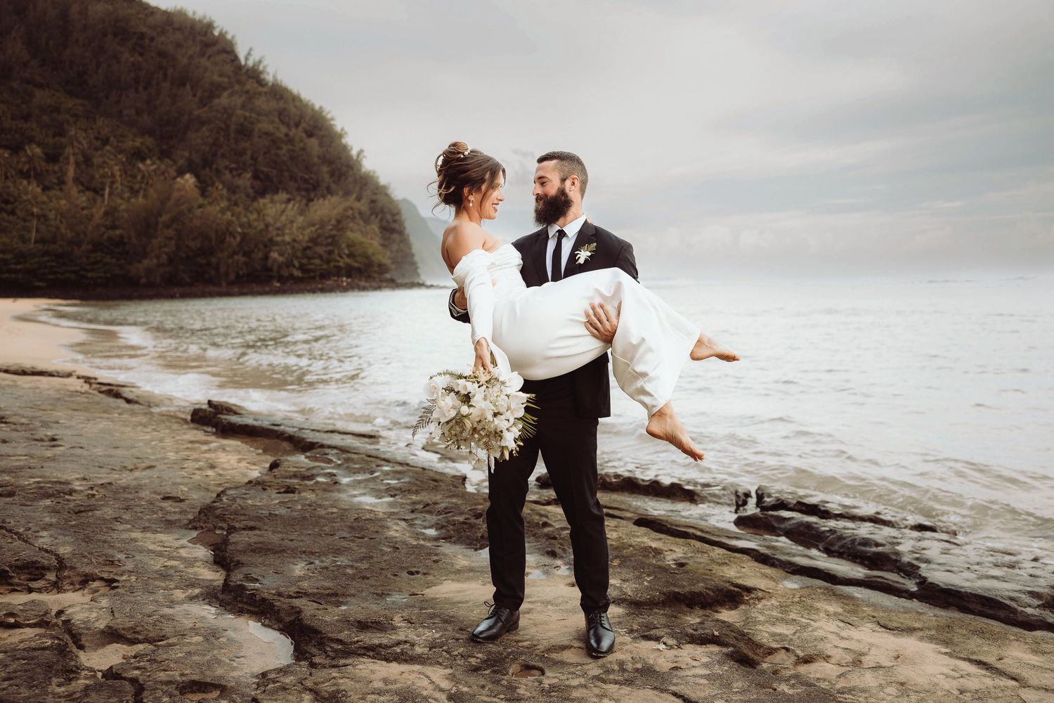 Groom puts bride on his shoulder after their beach elopement on the Na Pali coast in Kauai, Hawaii.