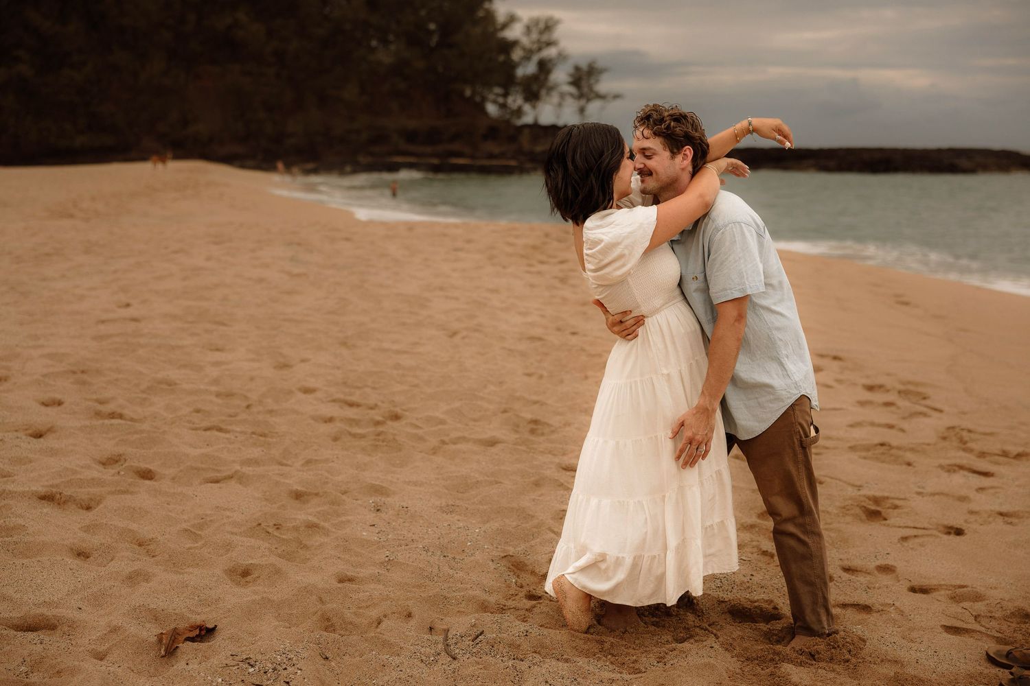 Girl wraps arms loosely around guys neck on the beach for engagement pictures in kauai, Hawaii.