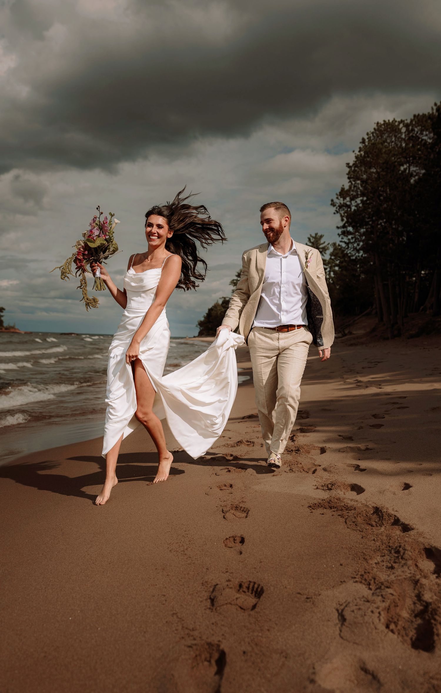 Bride and groom running on the beach following their elopement at Little Presque Isle in Marquette, Michigan, romantic beach ceremony