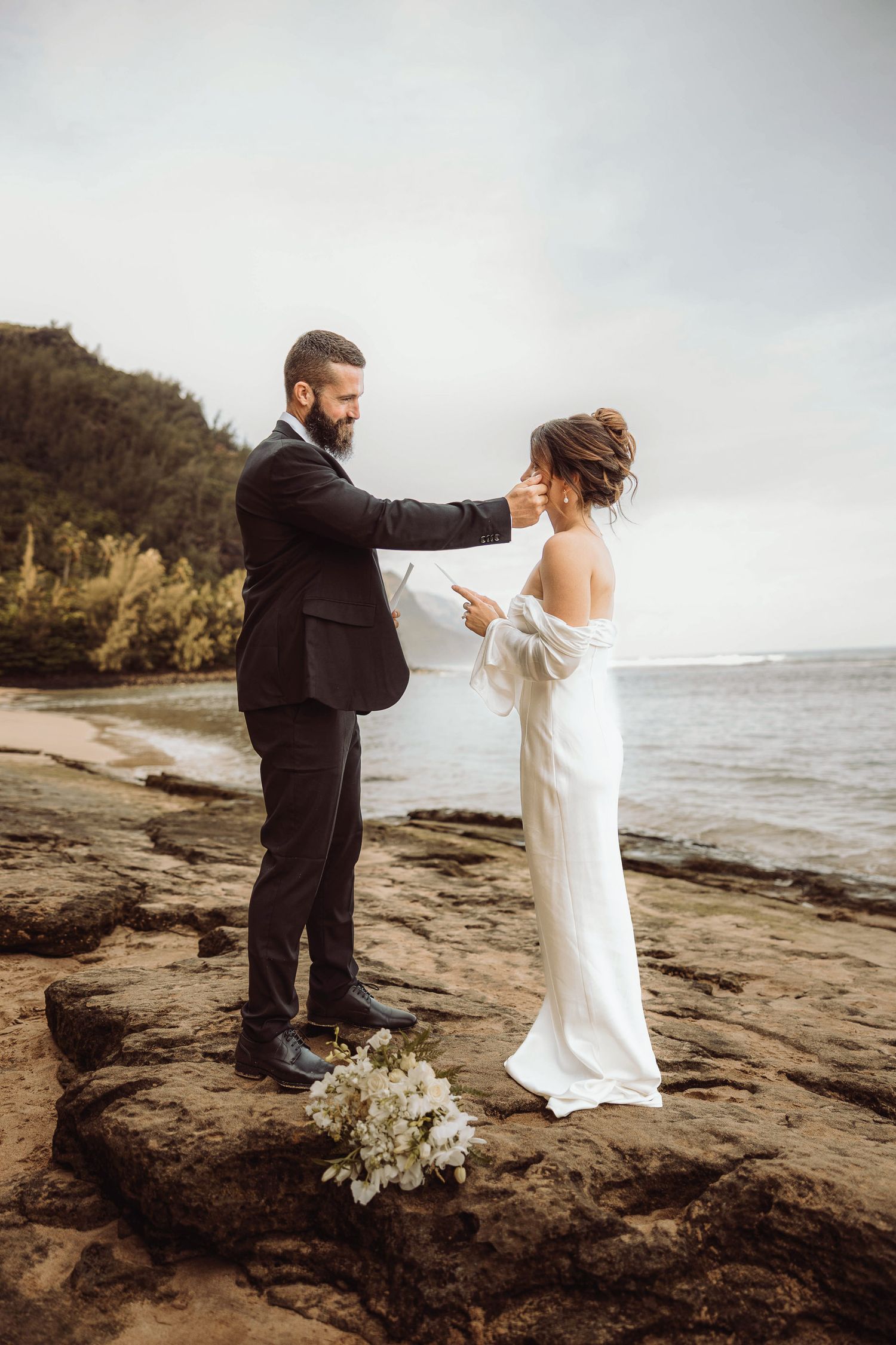 Groom puts bride on his shoulder after their beach elopement on the Na Pali coast in Kauai, Hawaii.
