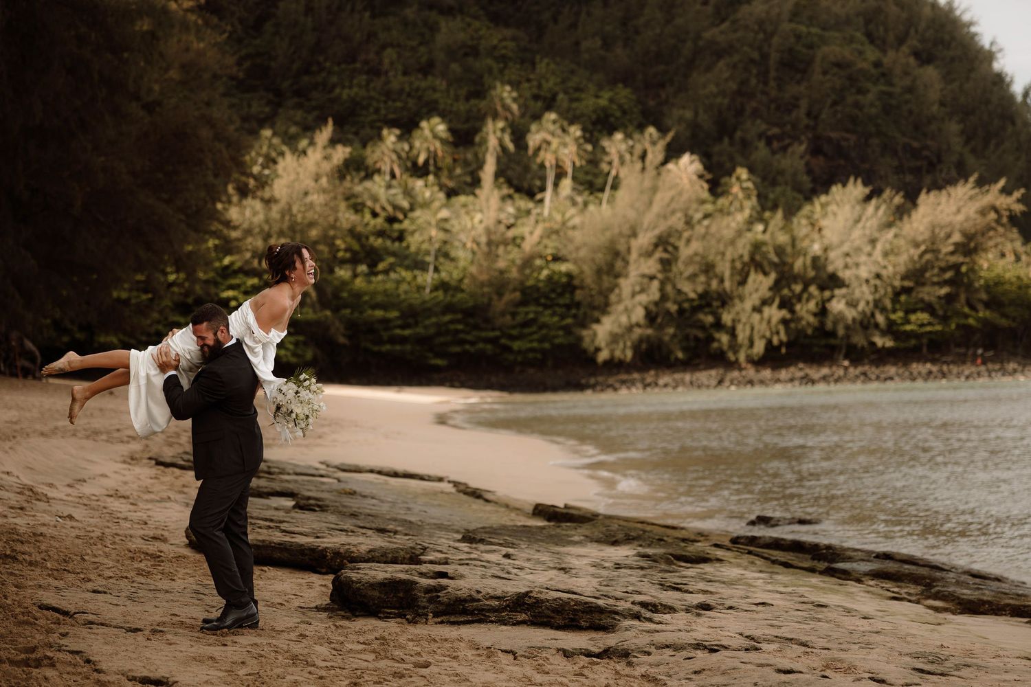 Groom puts bride on his shoulder after their beach elopement on the Na Pali coast in Kauai, Hawaii.