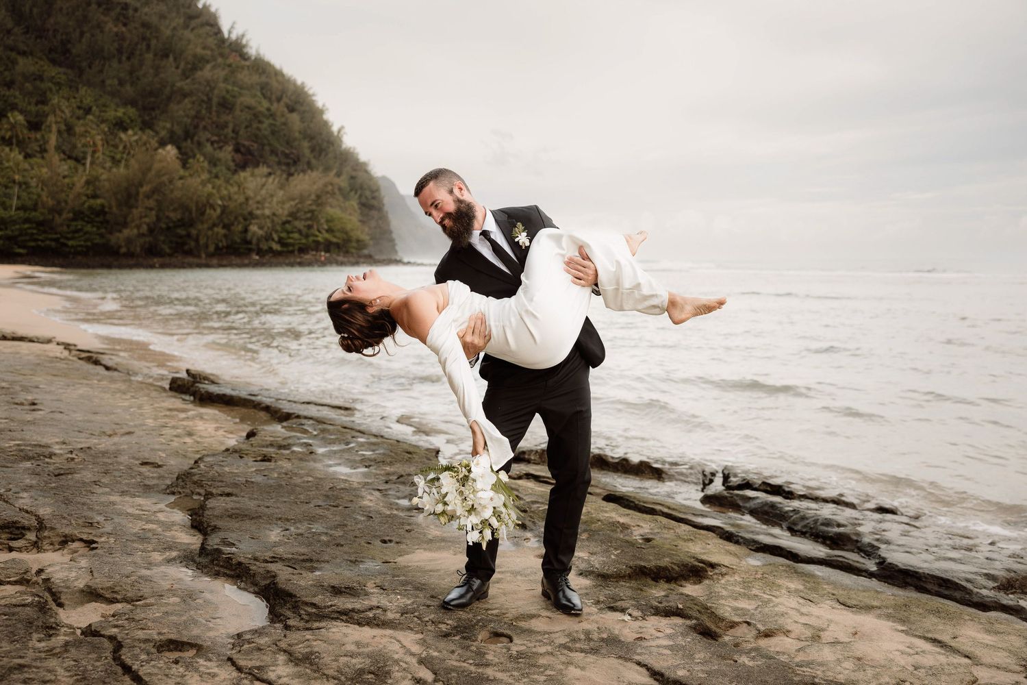 Groom dips the bride on the beach of an elopement on the Na Pali coast in Kauai, Hawaii.