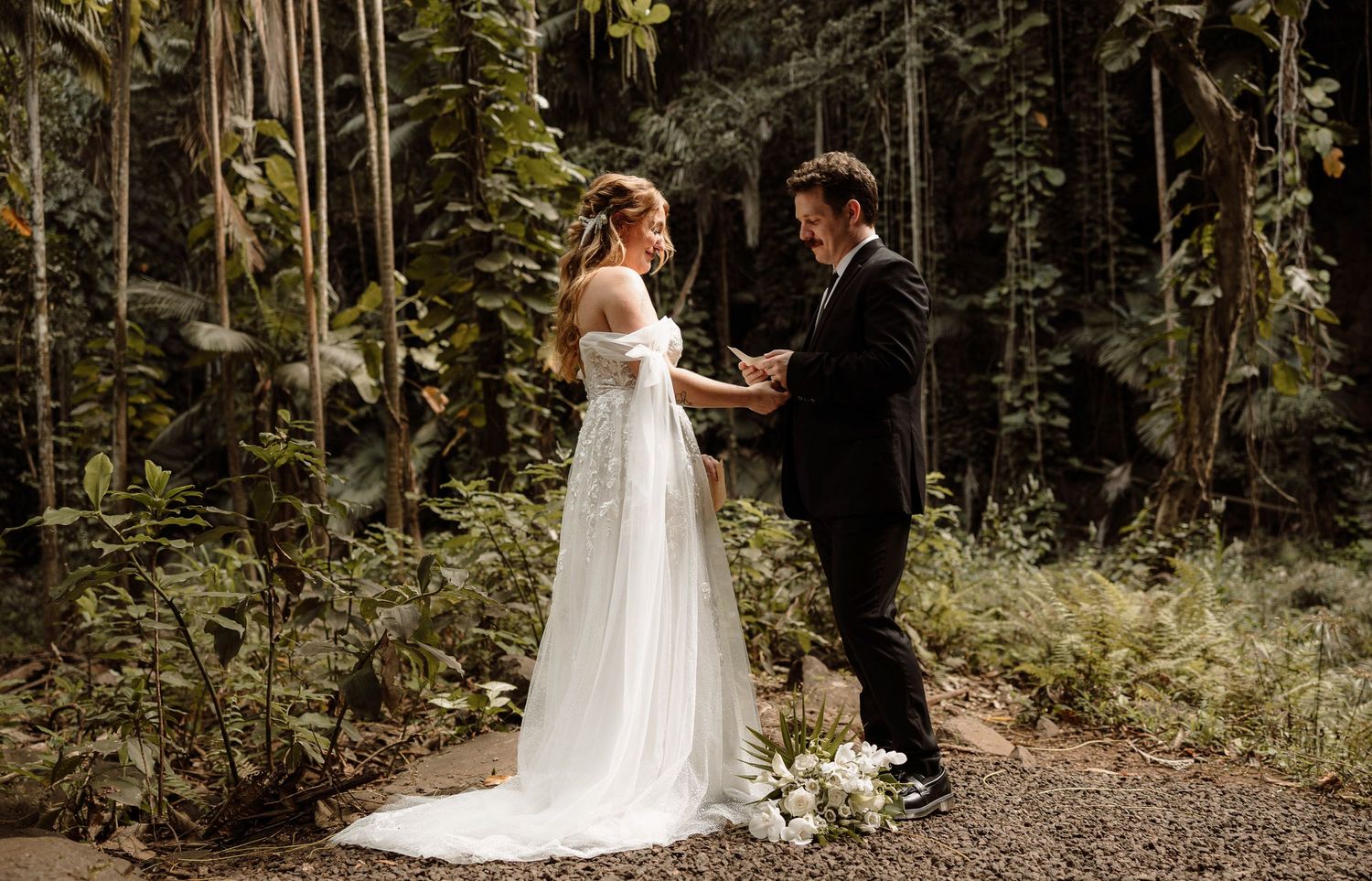 Bride and groom exchange vows in a botanical garden with a waterfall in Kauai, Hawaii