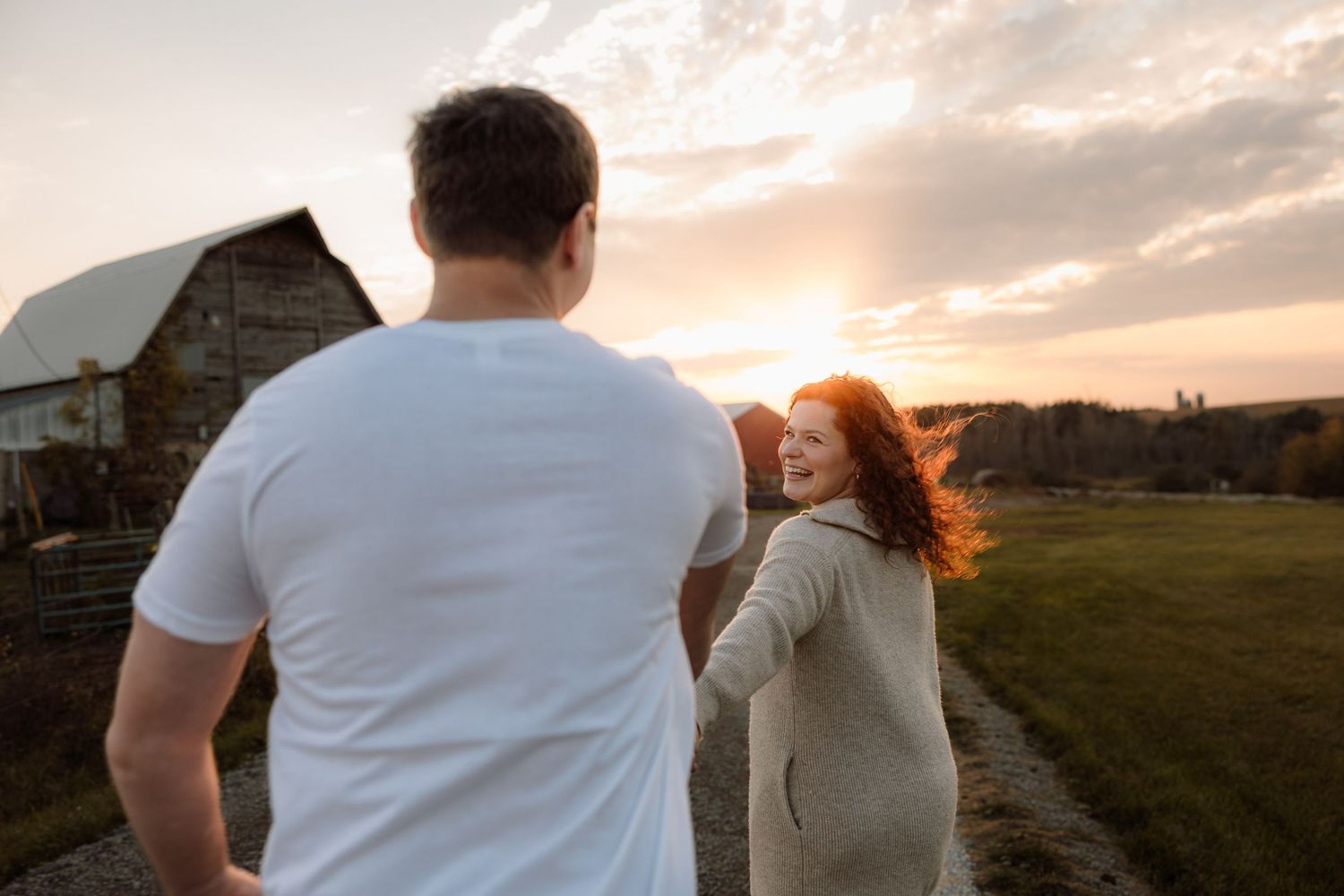 couple running with a barn in the background at golden hour for engagement pictures
