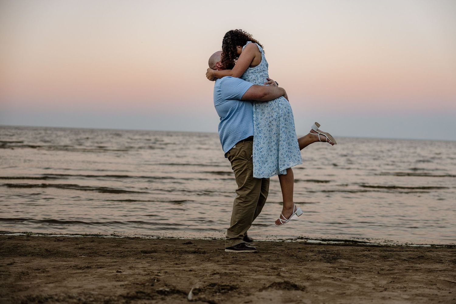 Beach engagement guy picks up girl and kissing on beach golden hour Marquette, Michigan.
