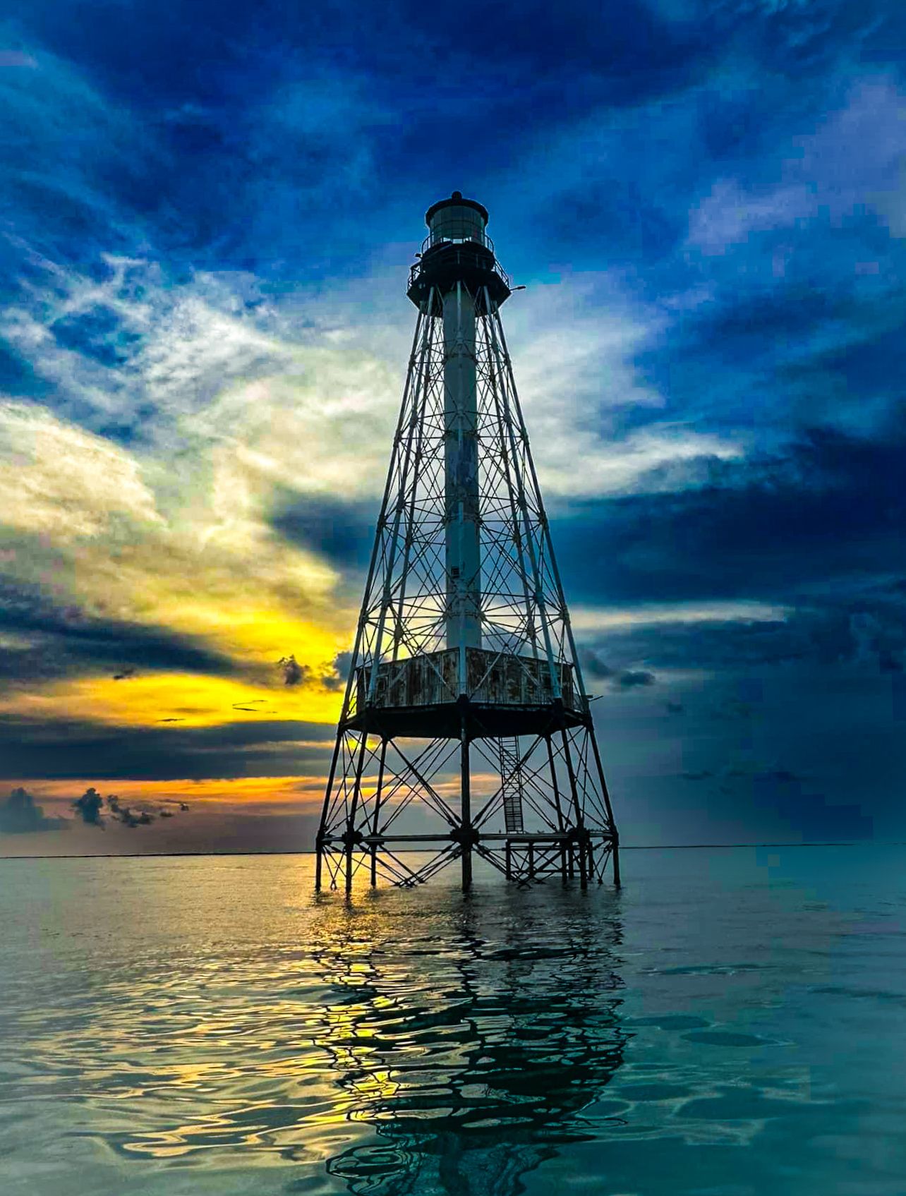 Silhouette of a historic Alligator lighthouse standing in calm ocean waters at dramatic colorful sunset.