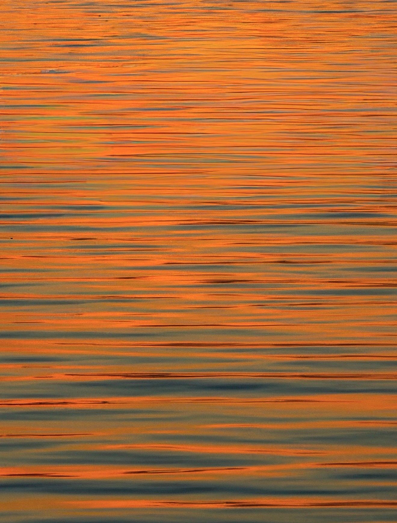 Rippling water reflecting vibrant orange and golden sunset light across calm ocean surface.