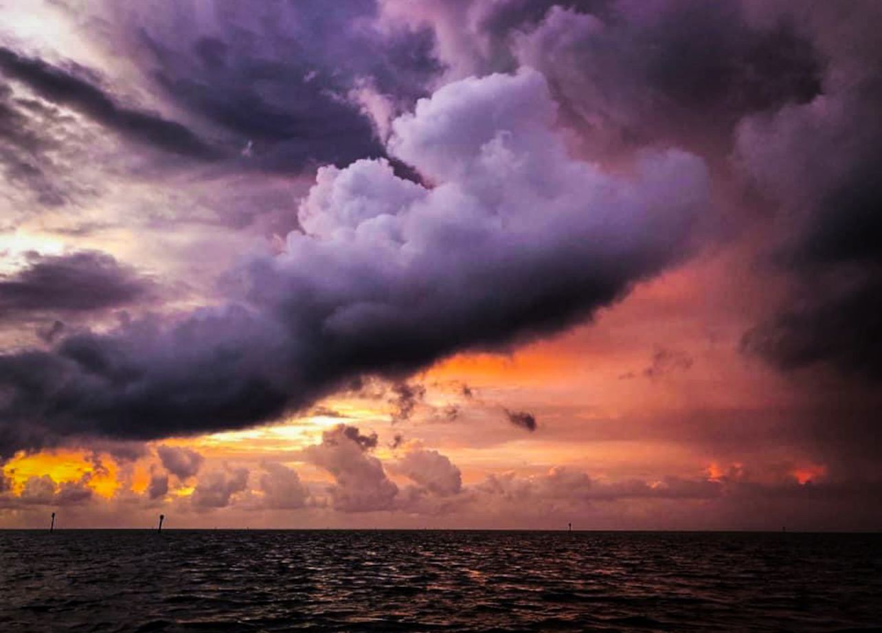 Dramatic storm clouds over ocean at sunset with vivid purple, pink, and golden hues illuminating the turbulent sky.