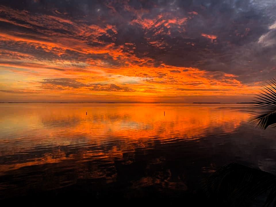Stunning fiery red and orange sunset reflecting over calm ocean waters with dramatic clouds.