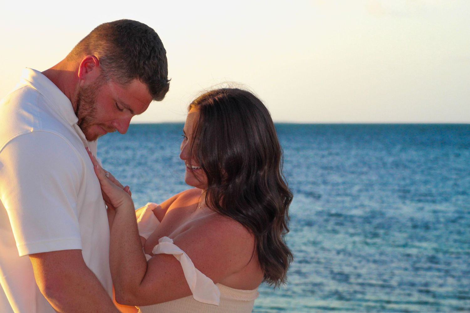 Couple embracing romantically on a tropical beach at sunset with turquoise ocean in the background.