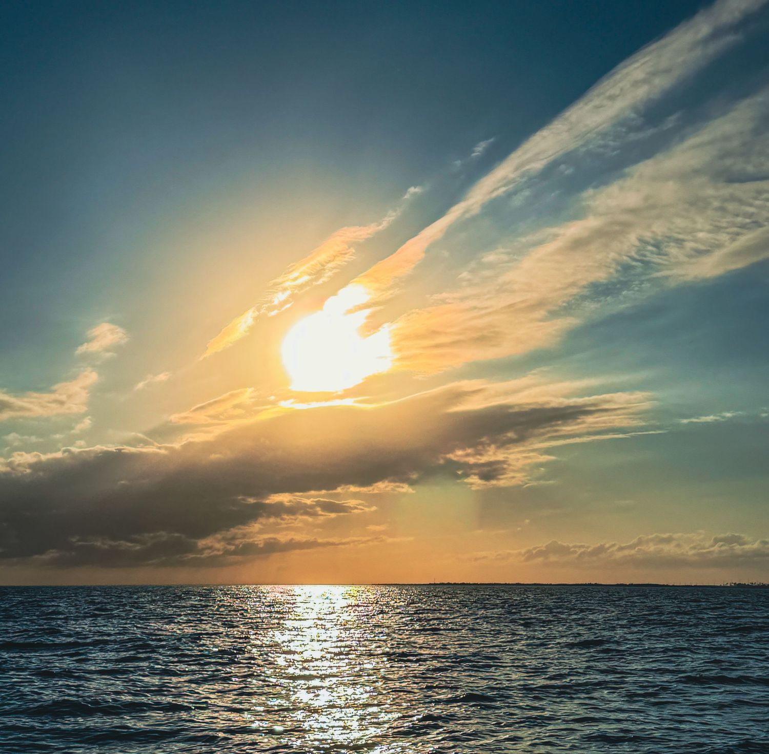 Golden sunset over calm ocean waters with dramatic clouds and sun rays reflecting on the sea surface.