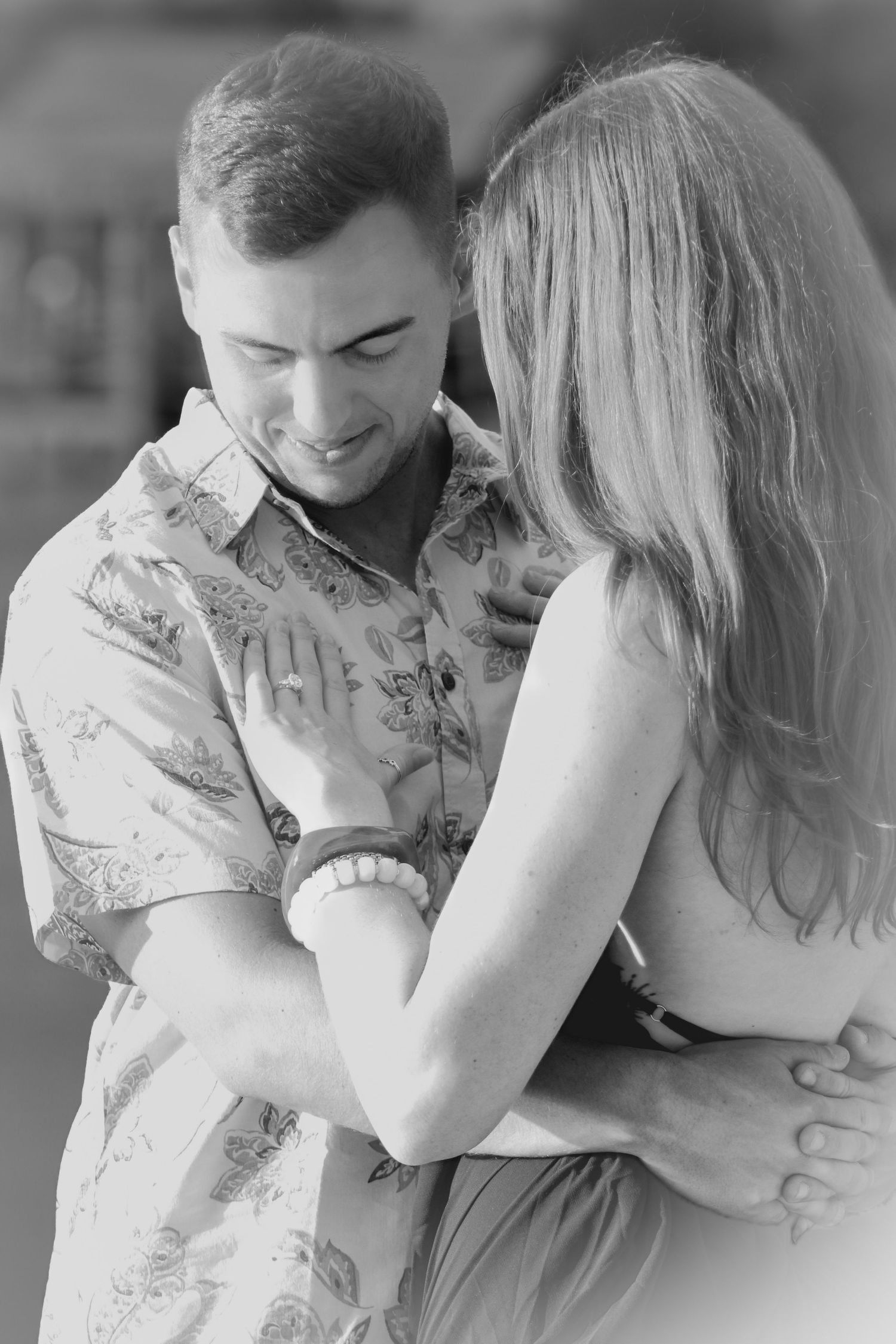 Black and white photo of a couple embracing tenderly, man in floral shirt smiling down at woman with long blonde hair.