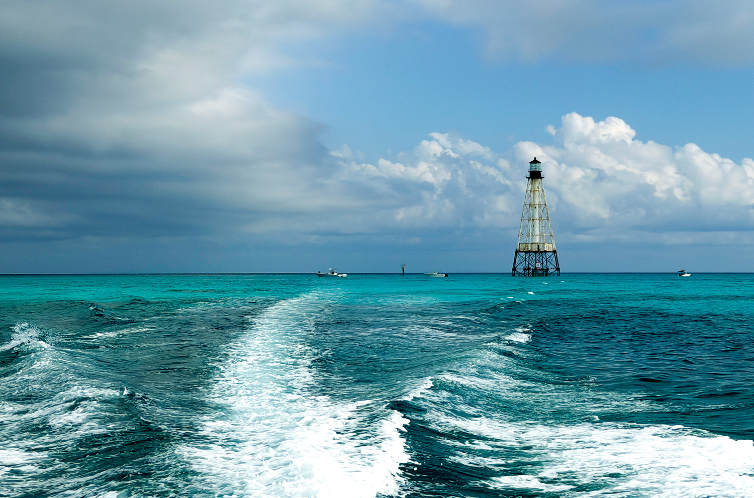 Boat wake leads to a offshore lighthouse on turquoise waters under dramatic cloudy skies in the Florida Keys.