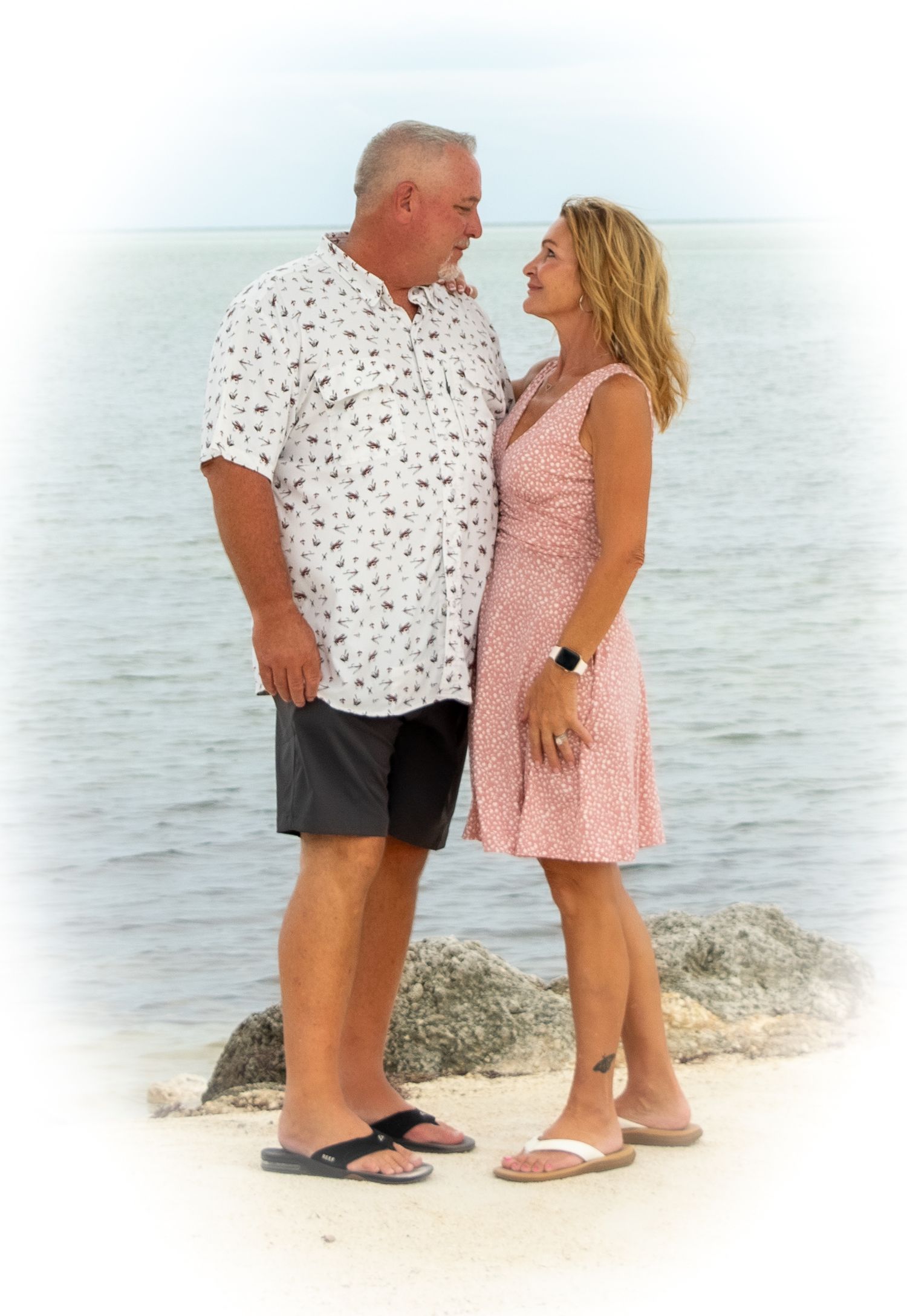 Couple sharing a romantic moment on a rocky beach shore with ocean waves in the background.