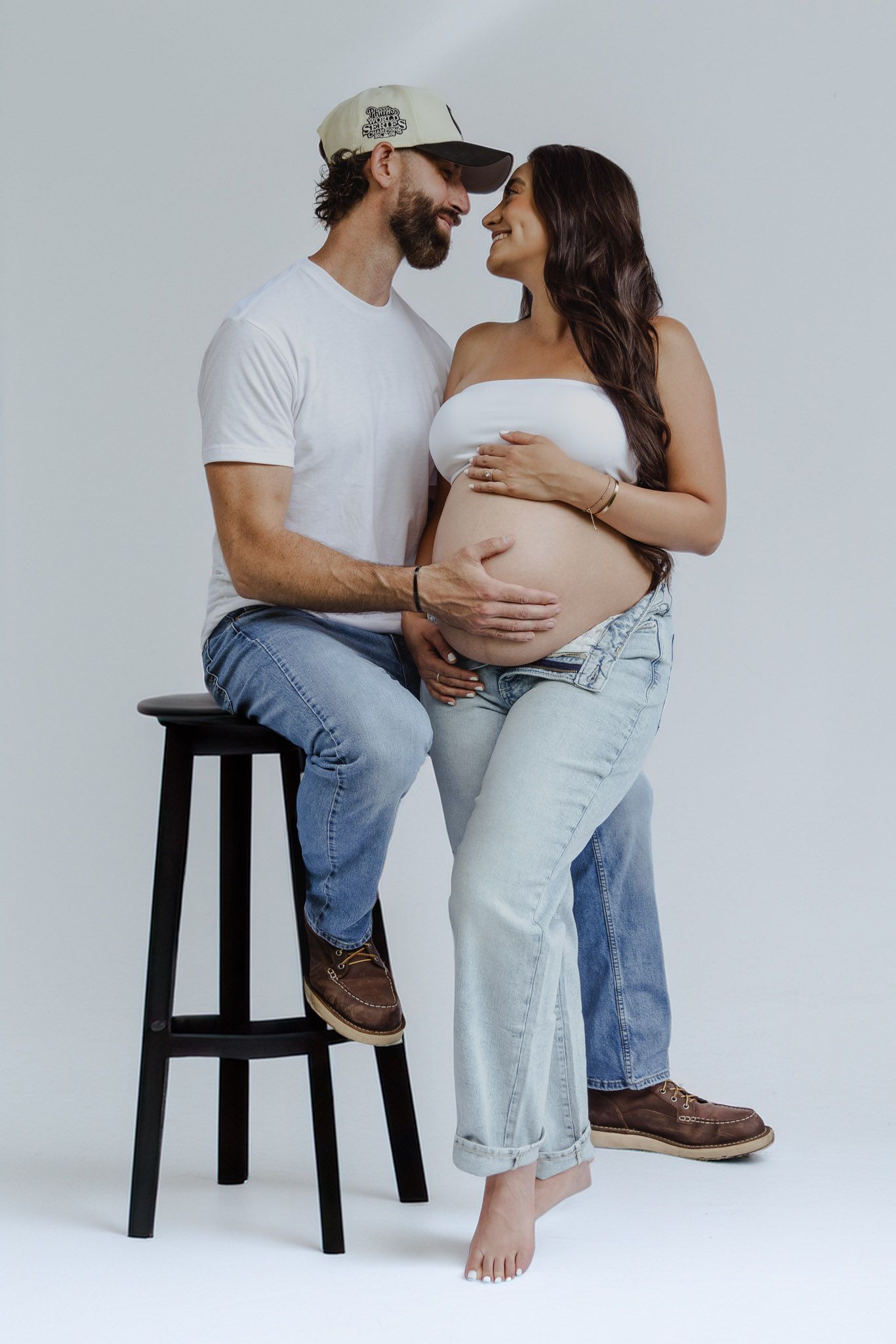 Minimalist studio maternity session with couple in casual wear sharing tender moments.