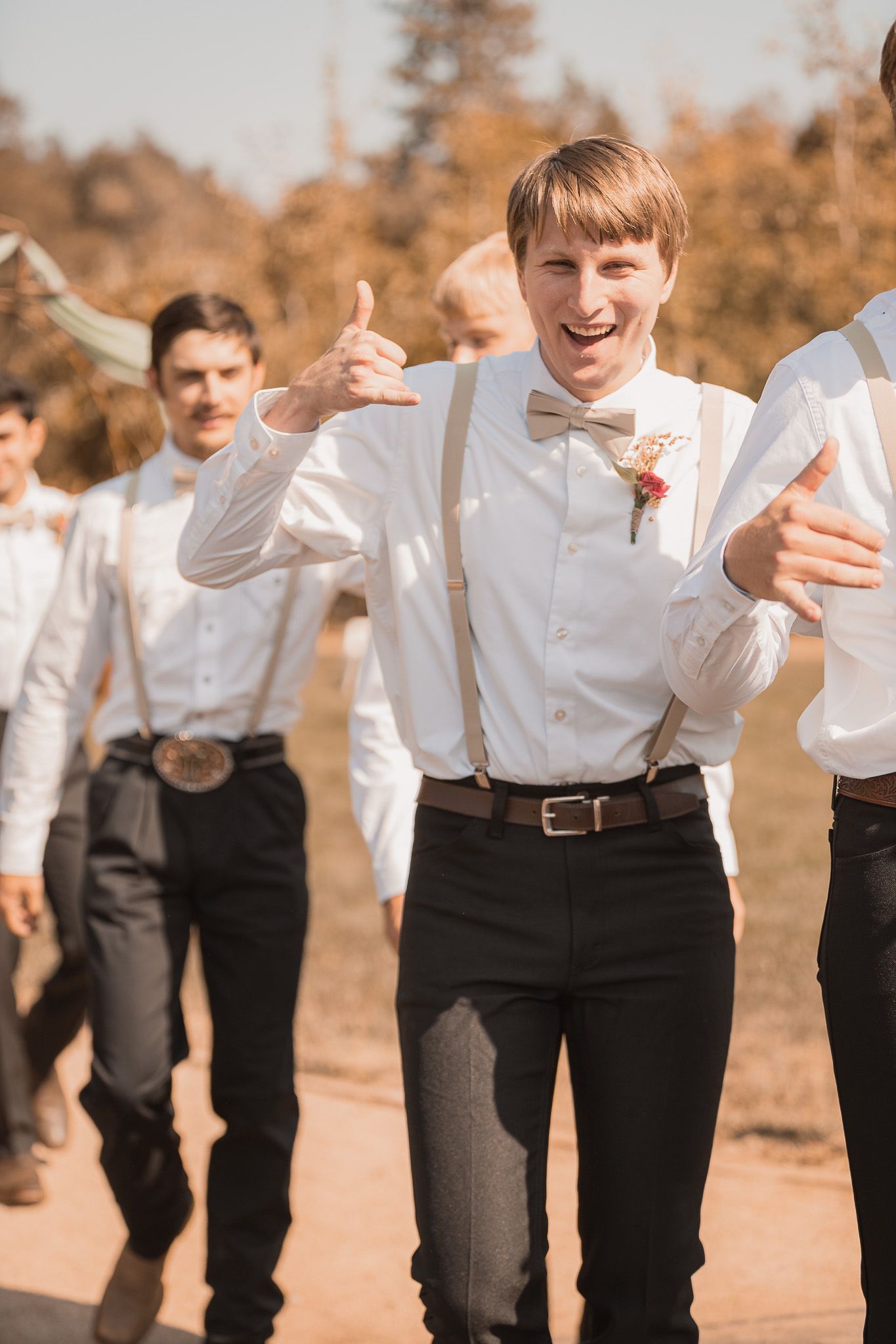 Young boys in white shirts and black pants run playfully in a line outdoors.