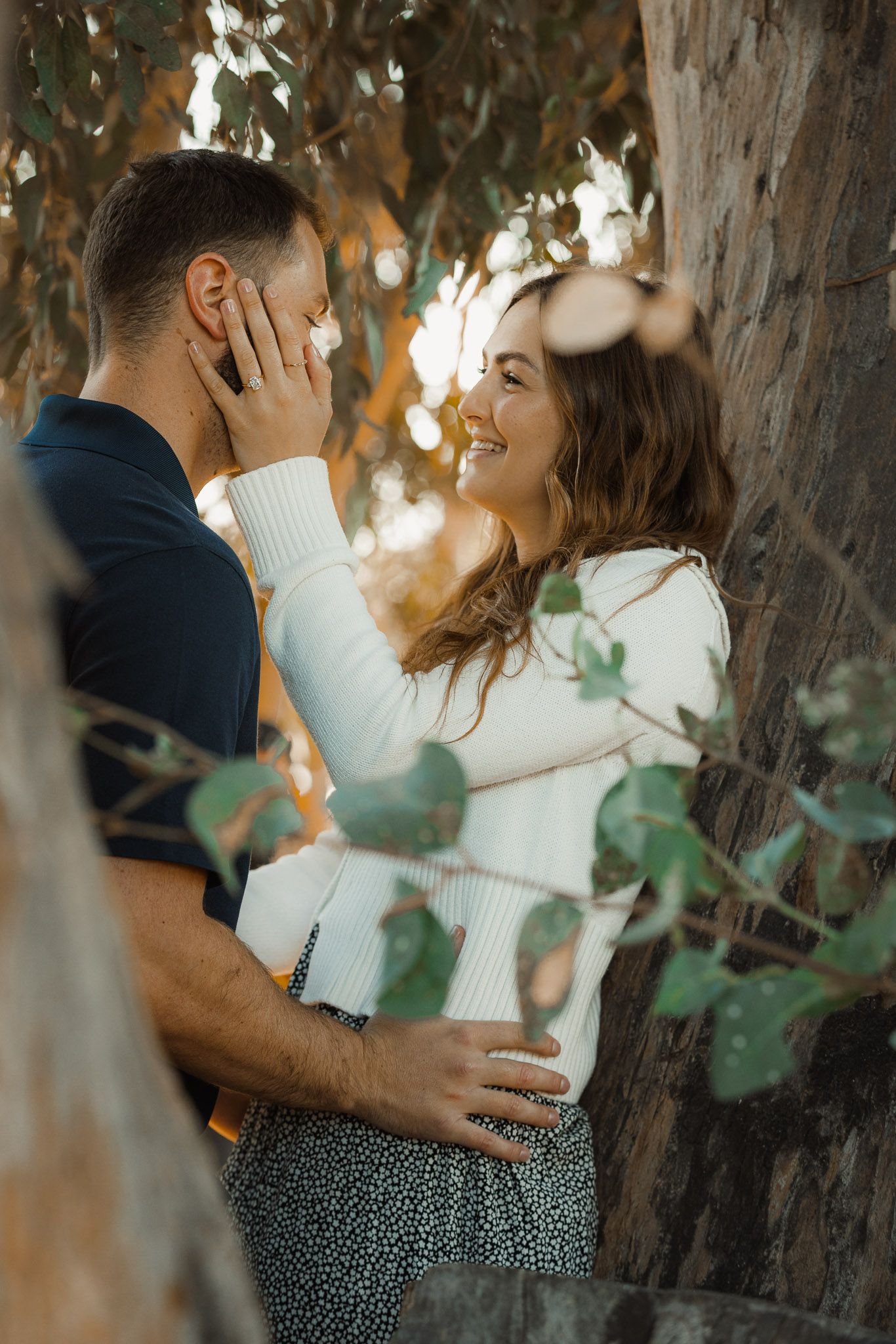 Couple sharing intimate moment among tree branches in golden sunlight.