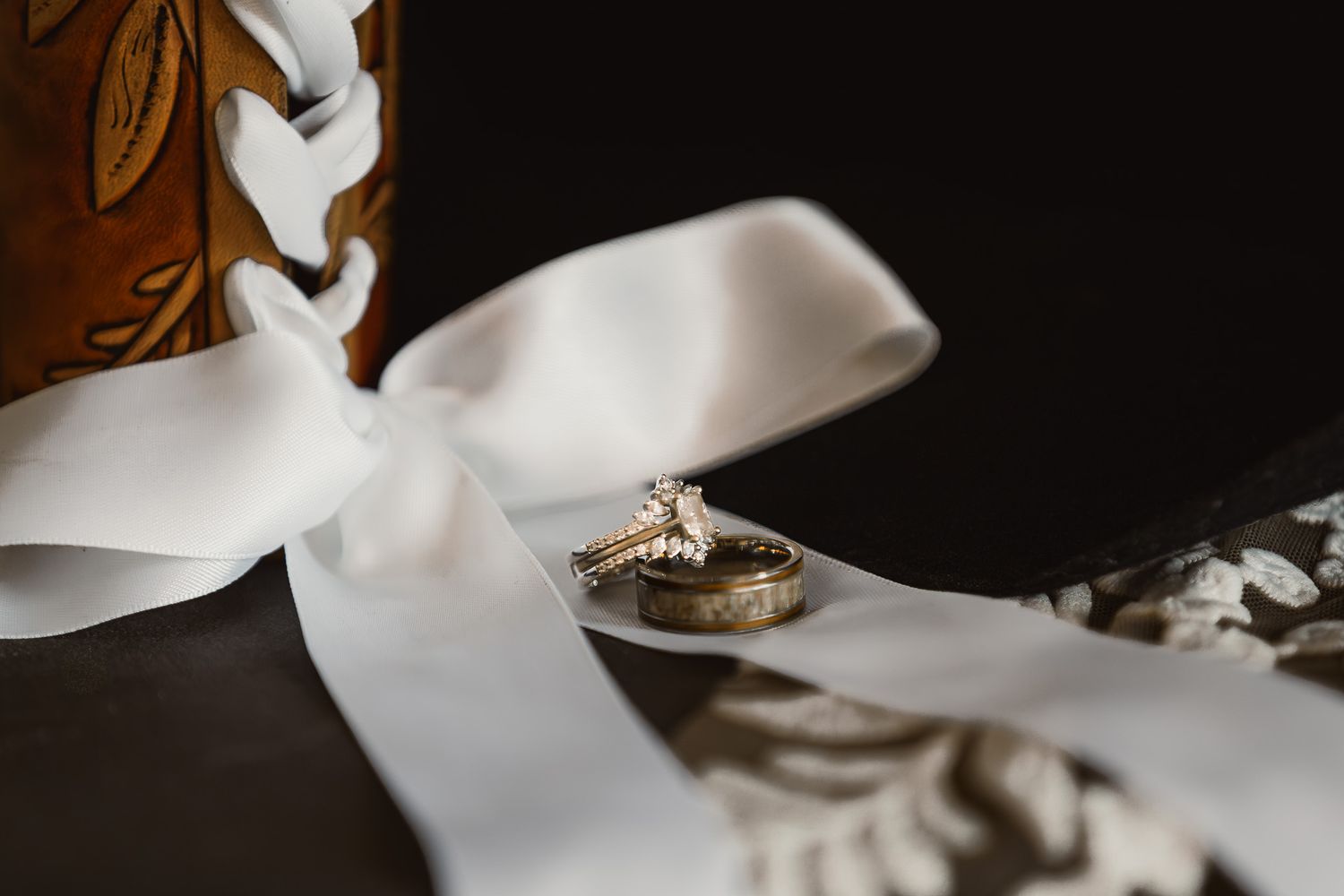 Wedding rings displayed with white ribbon on dark background.