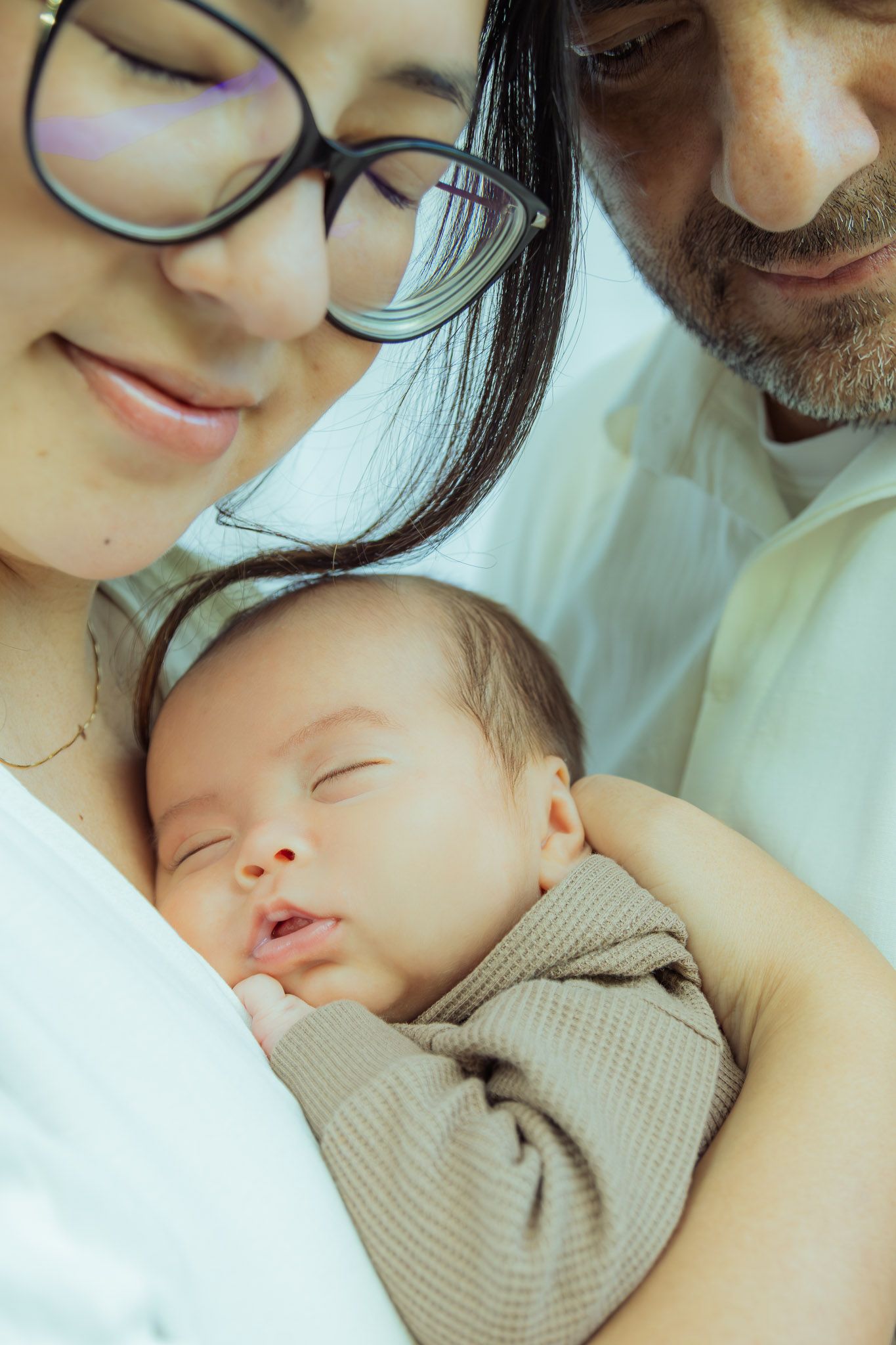 A sleeping baby in a beige sweater rests peacefully against someone's chest in a tender family moment.