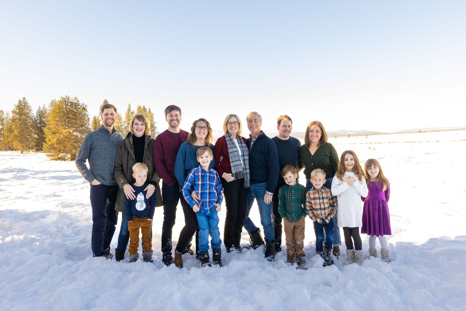 A group of people standing together in snowy winter landscape during sunset with mountains in background.