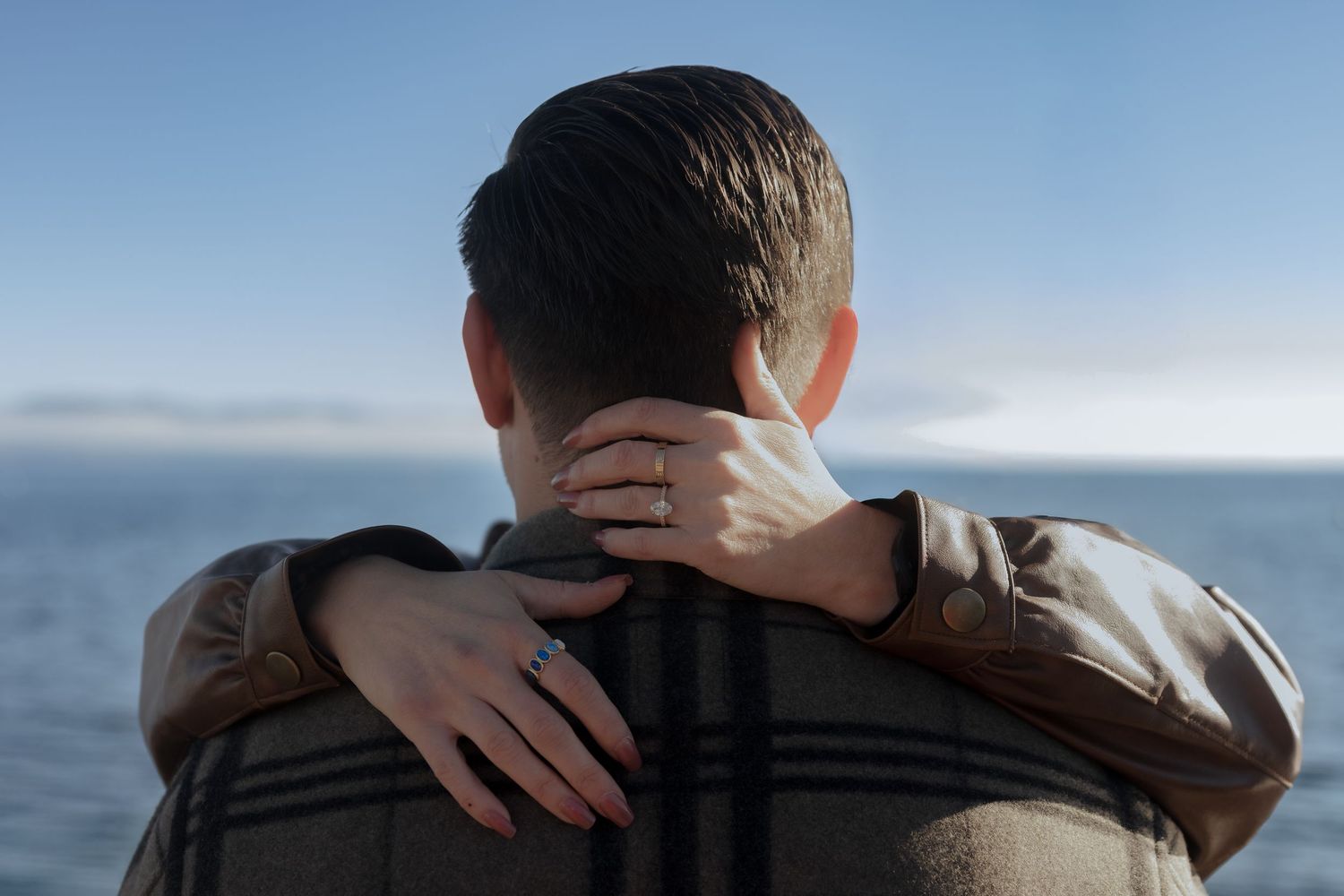A close-up view of two people hugging outdoors with a blurred natural background.