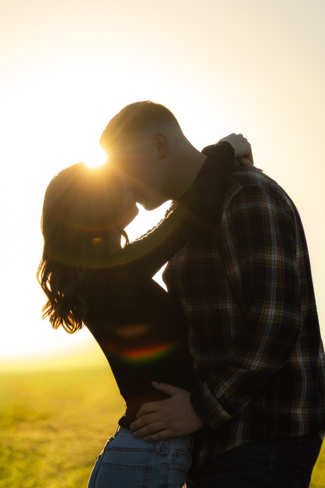 Silhouette of couple embracing against sunset in field.
