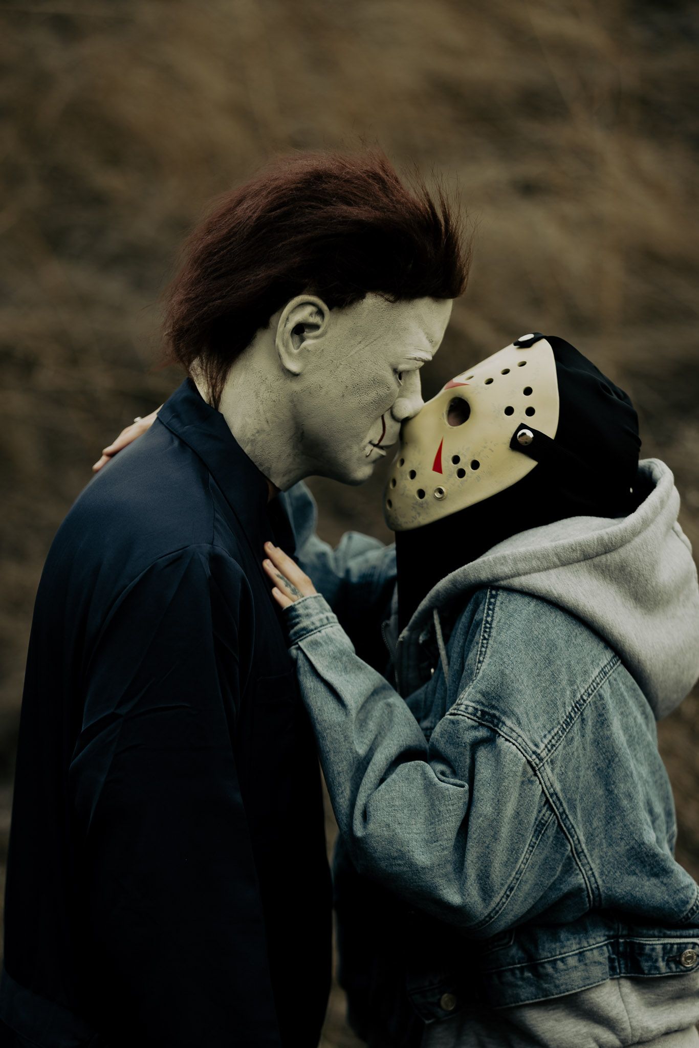 Close-up shot of two people in dark clothing sharing an intimate moment while one wears a hockey mask.