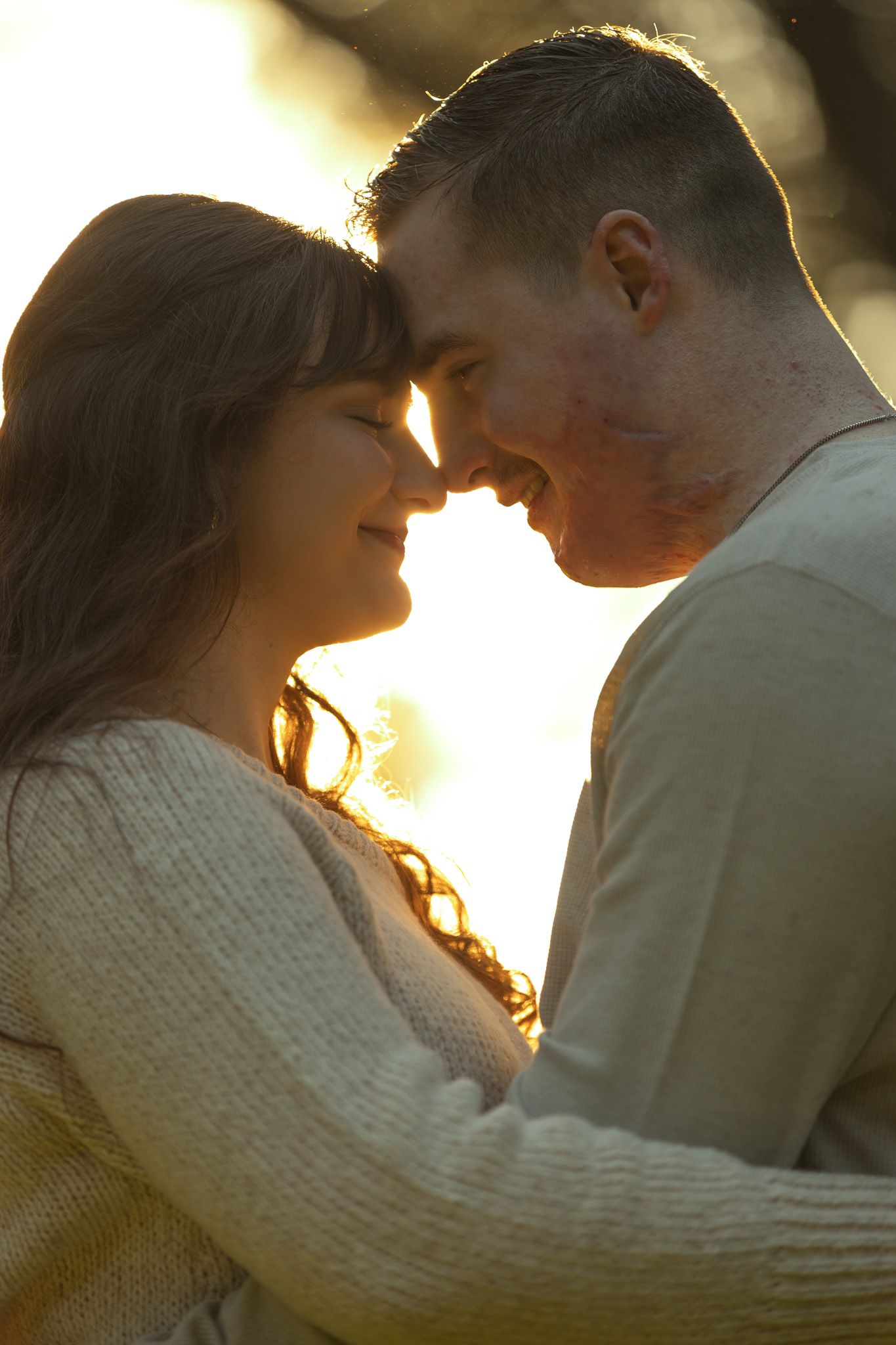 A romantic couple shares an intimate moment at sunset with golden backlighting creating a warm silhouette effect.