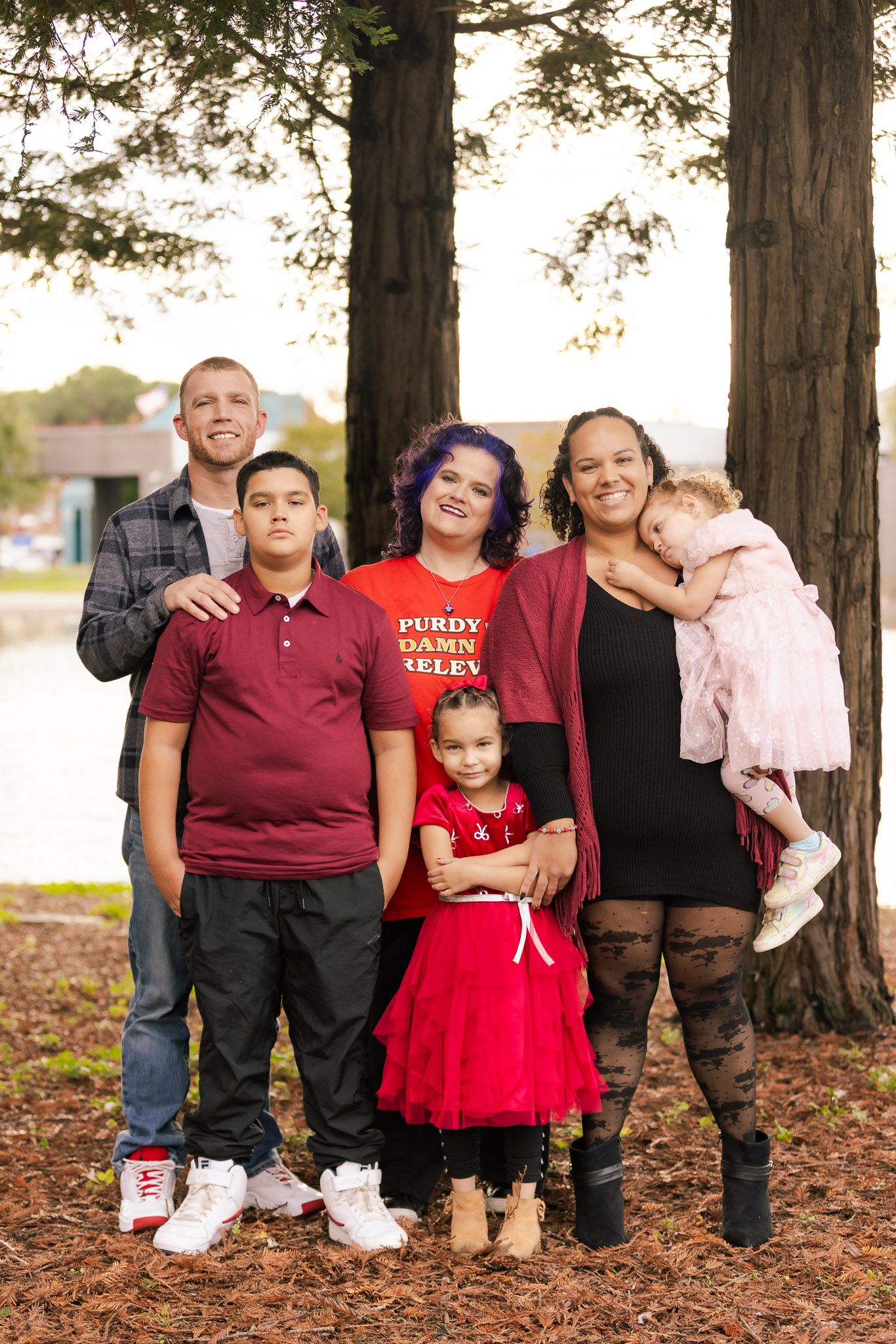Family group portrait taken outdoors under tall trees with everyone wearing red and black coordinated outfits.