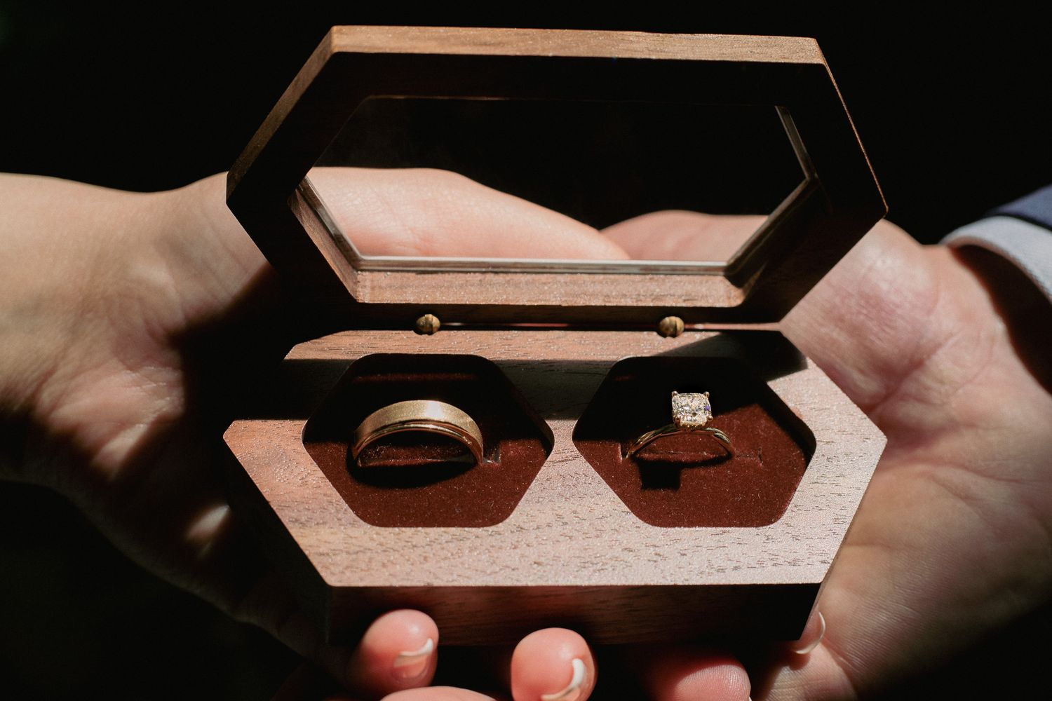 Wooden ring box being opened to reveal wedding rings in dramatic lighting.
