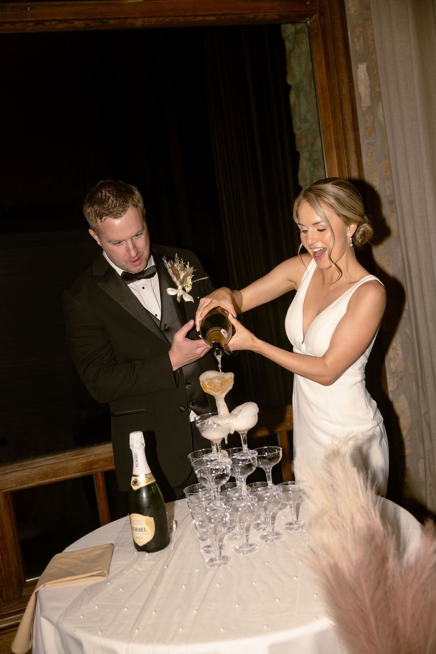 Bride and groom pouring champagne tower at wedding reception, elegant white gown and black tuxedo.