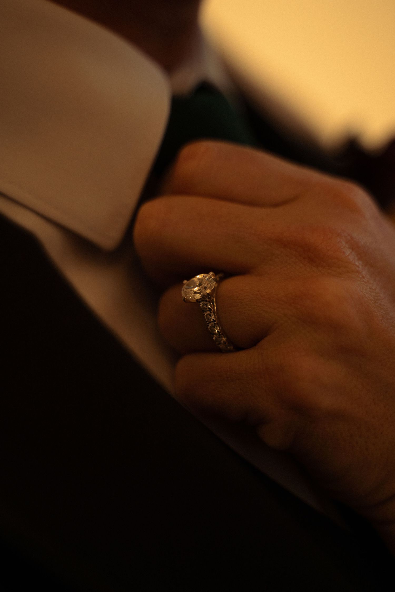Close-up of a diamond engagement ring on a woman's finger, worn against a man's dark suit jacket.